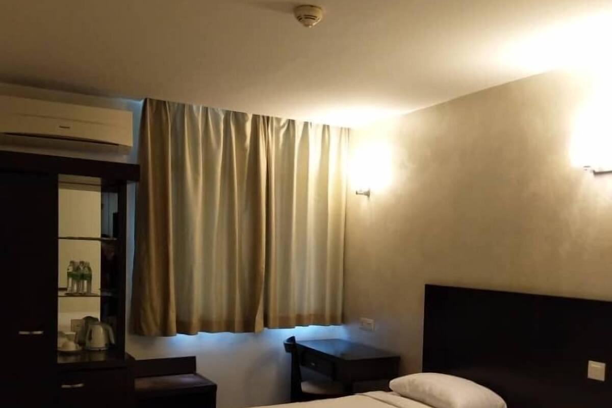 A hotel room with two single beds, a desk, a chair, a wardrobe, and a window with curtains.