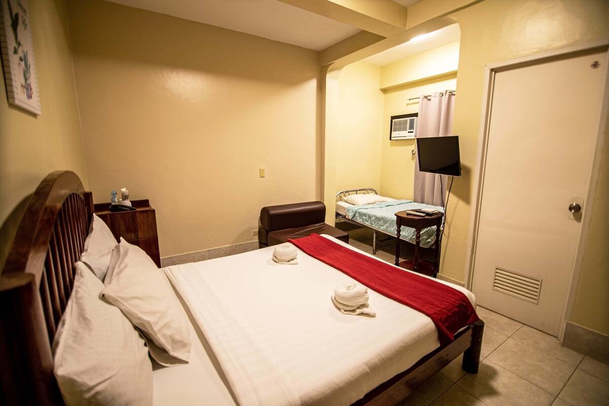 A hotel room with a bed, a desk, a chair, a television, and a door.