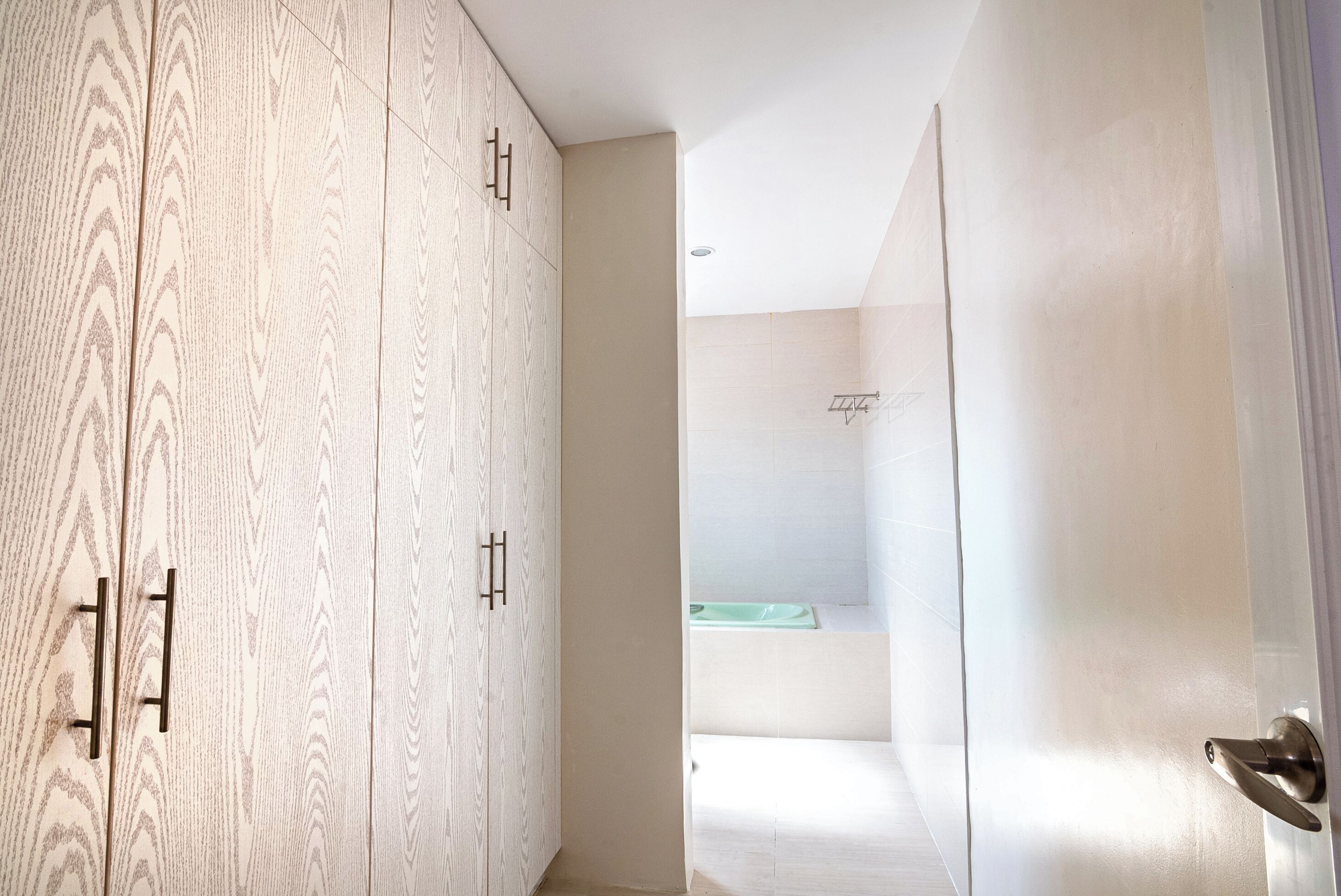 A hallway with a wooden wardrobe, a bathroom with a green sink, and a white door.