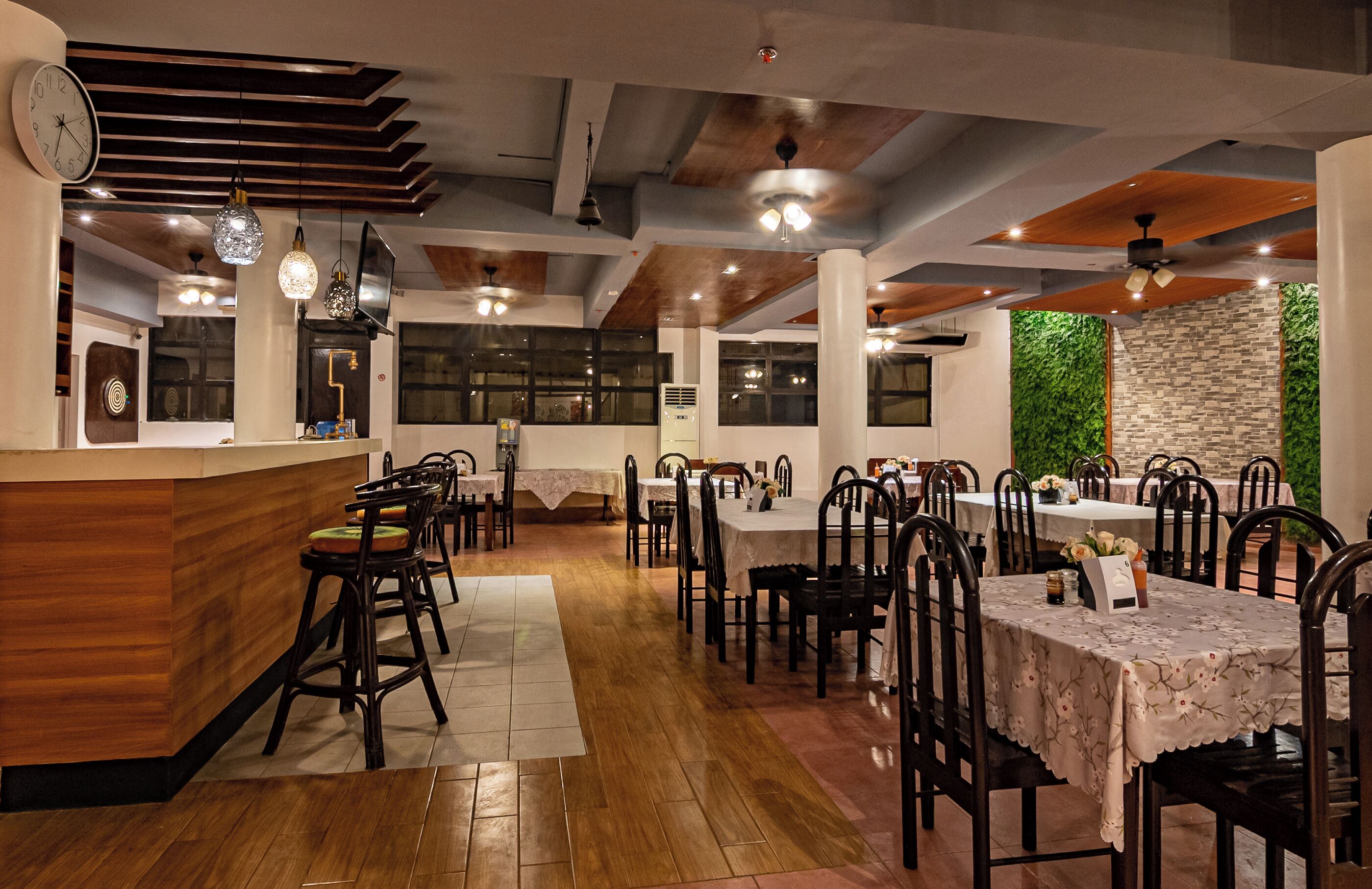 A restaurant with wooden flooring, tables with white tablecloths, and hanging pendant lights.