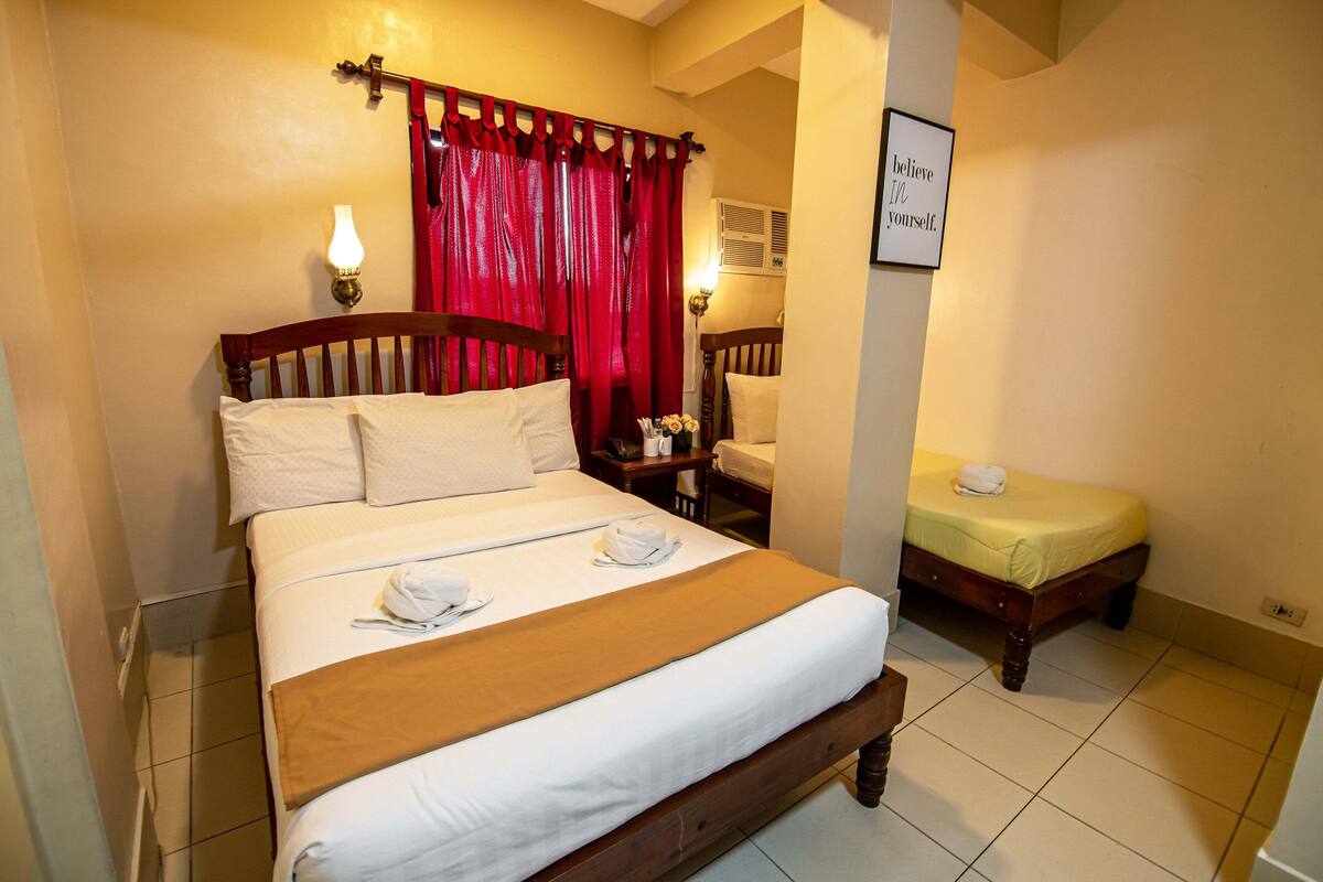 A hotel room with a large bed, a smaller bed, a nightstand with a lamp, and a wall-mounted sign.