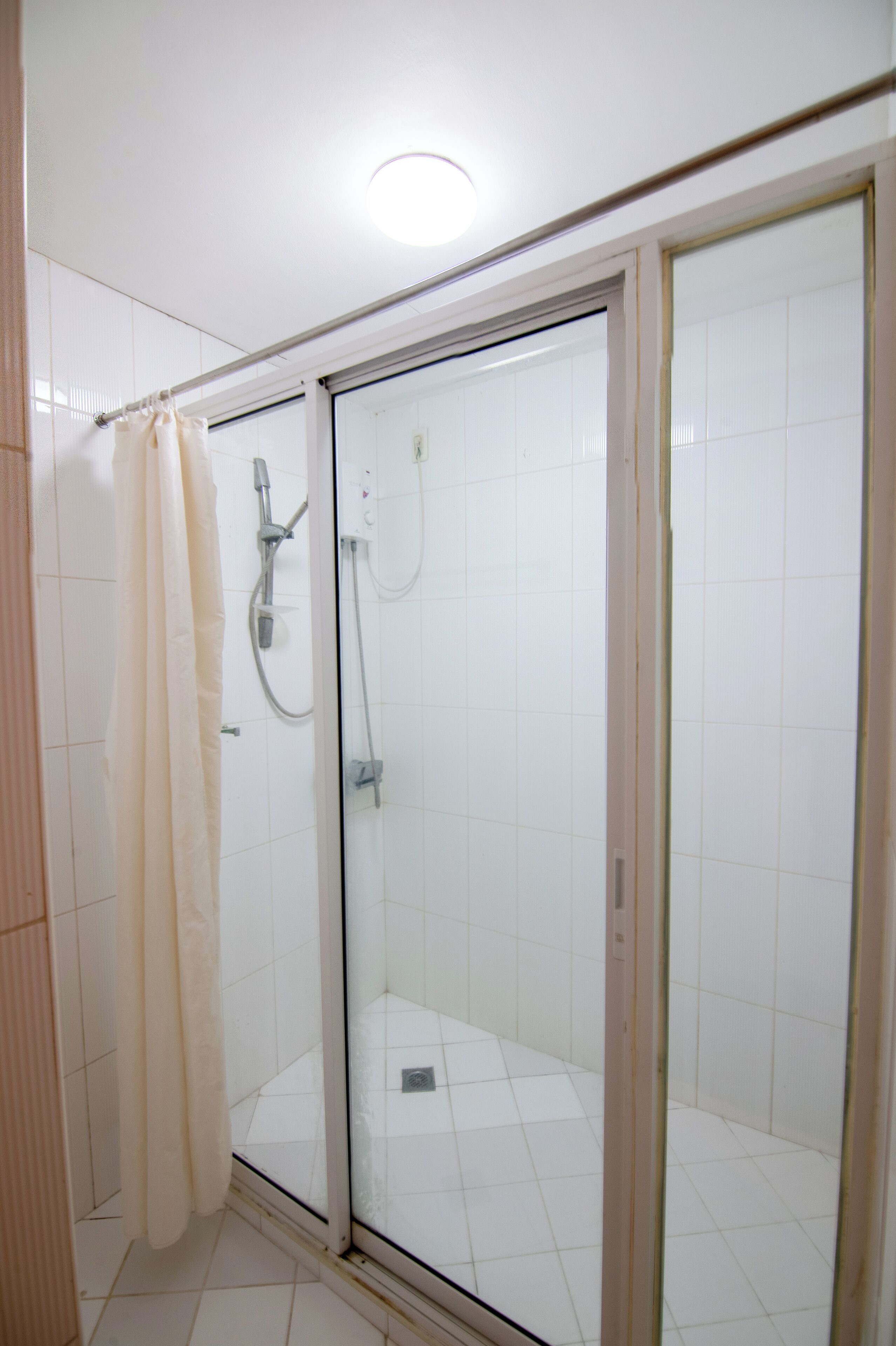 A glass-enclosed shower with a showerhead and control panel, a curtain, and tiled walls.