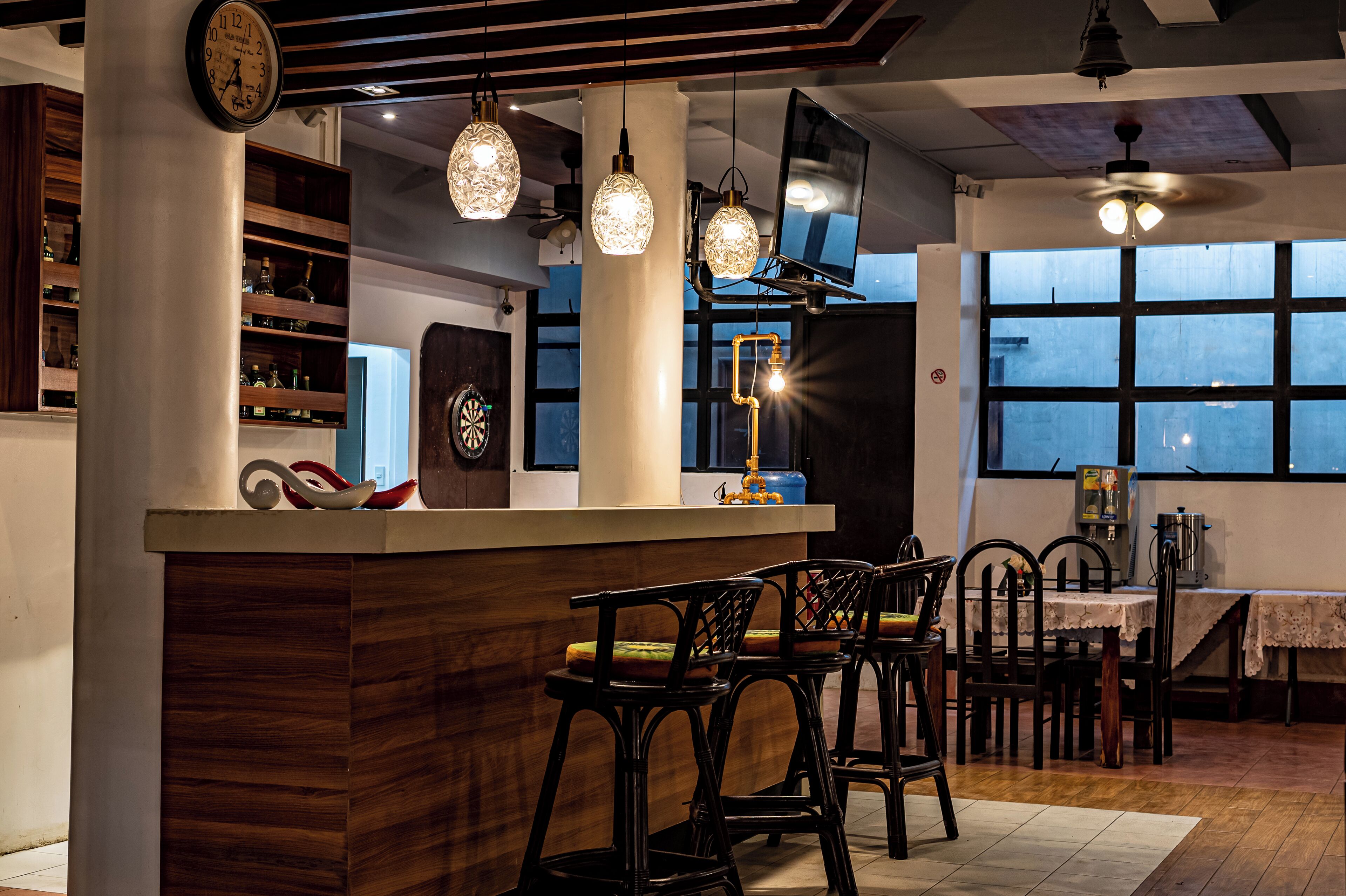 A bar area with a wooden counter, hanging light fixtures, and bar stools.