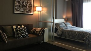 A modern hotel room with a sofa, a bed with patterned bedding, a wall art piece, and a floor lamp. - dcondo mine by BP (Kathu)