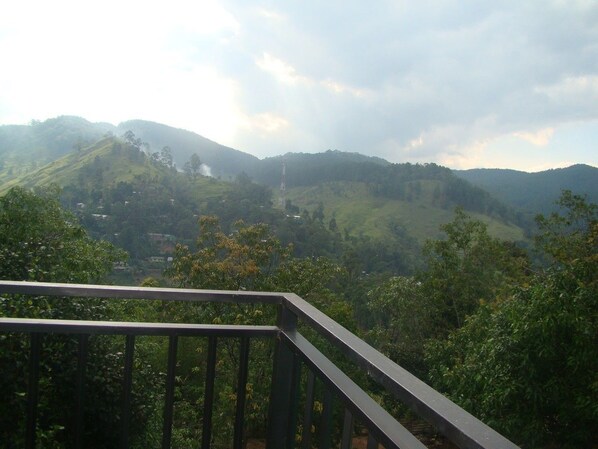 Vista desde un balcón sobre un paisaje montañoso con una torre al lejos.