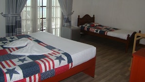 Habitación con dos camas, una más grande y otra más pequeña, ambas con ropa de cama decorada con la bandera estadounidense. Hay un televisor en la pared y una lámpara colgando sobre la cama más pequeña.