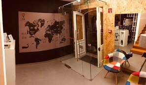 Een hotel lobby met een wereldkaart aan de muur, een glazen ingang en kleurrijke stoelen.