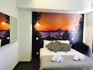 Hotelkamer met een bed, nachtkastje, stoel en een muurschildering van een berg bij zonsondergang.