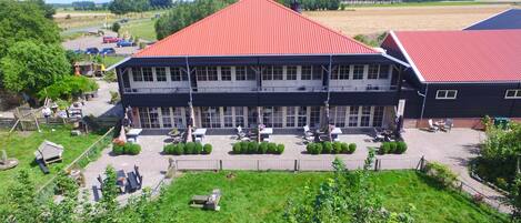 A two-story building with a red roof, large windows, and a paved courtyard with outdoor seating.