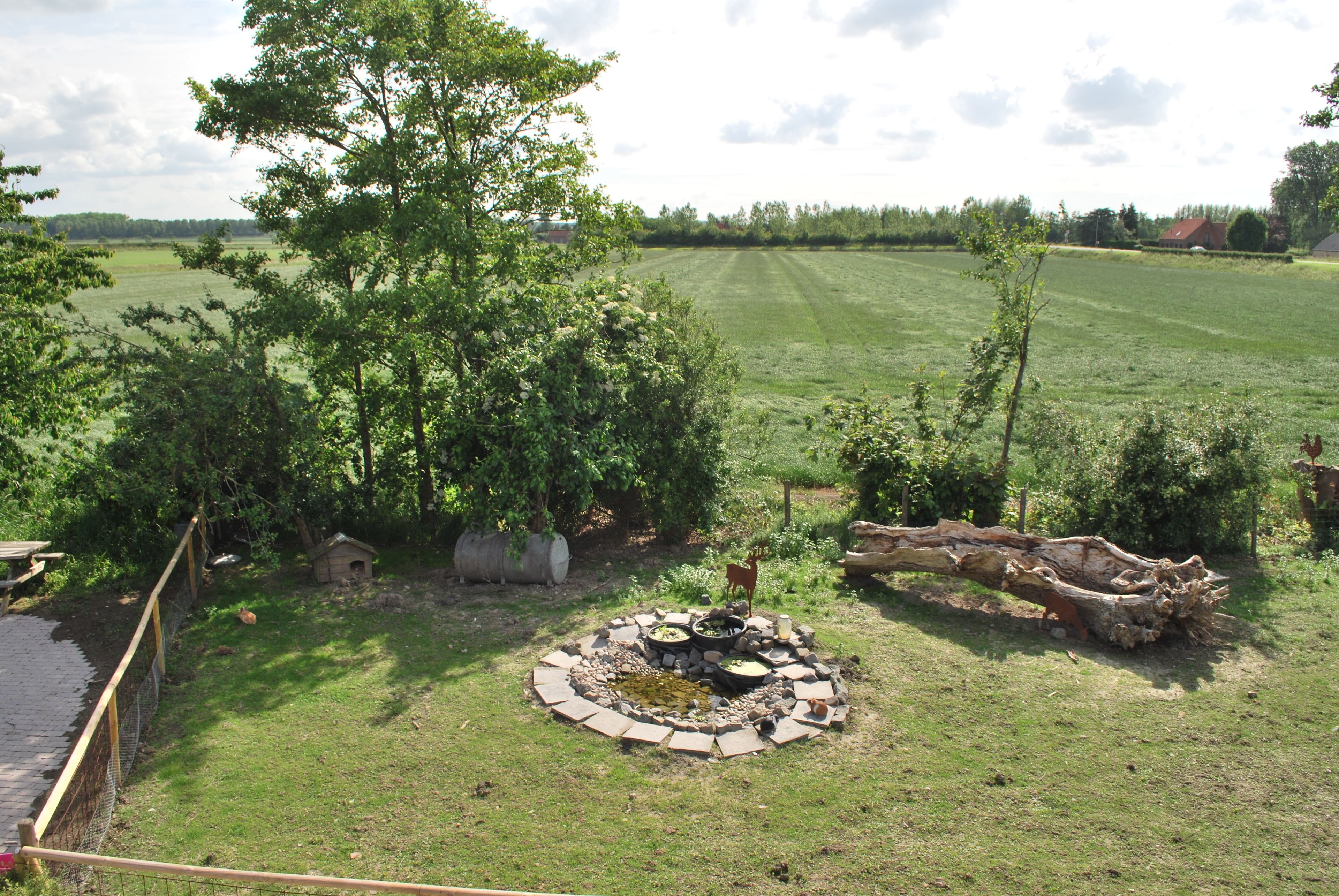 Un foyer circulaire en pierre, entouré d’une bordure de pierres, avec un banc en bois et un petit nichoir à proximité.