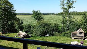 A rural landscape with a wooden structure, possibly a barn, and a fenced area with a table and chairs.