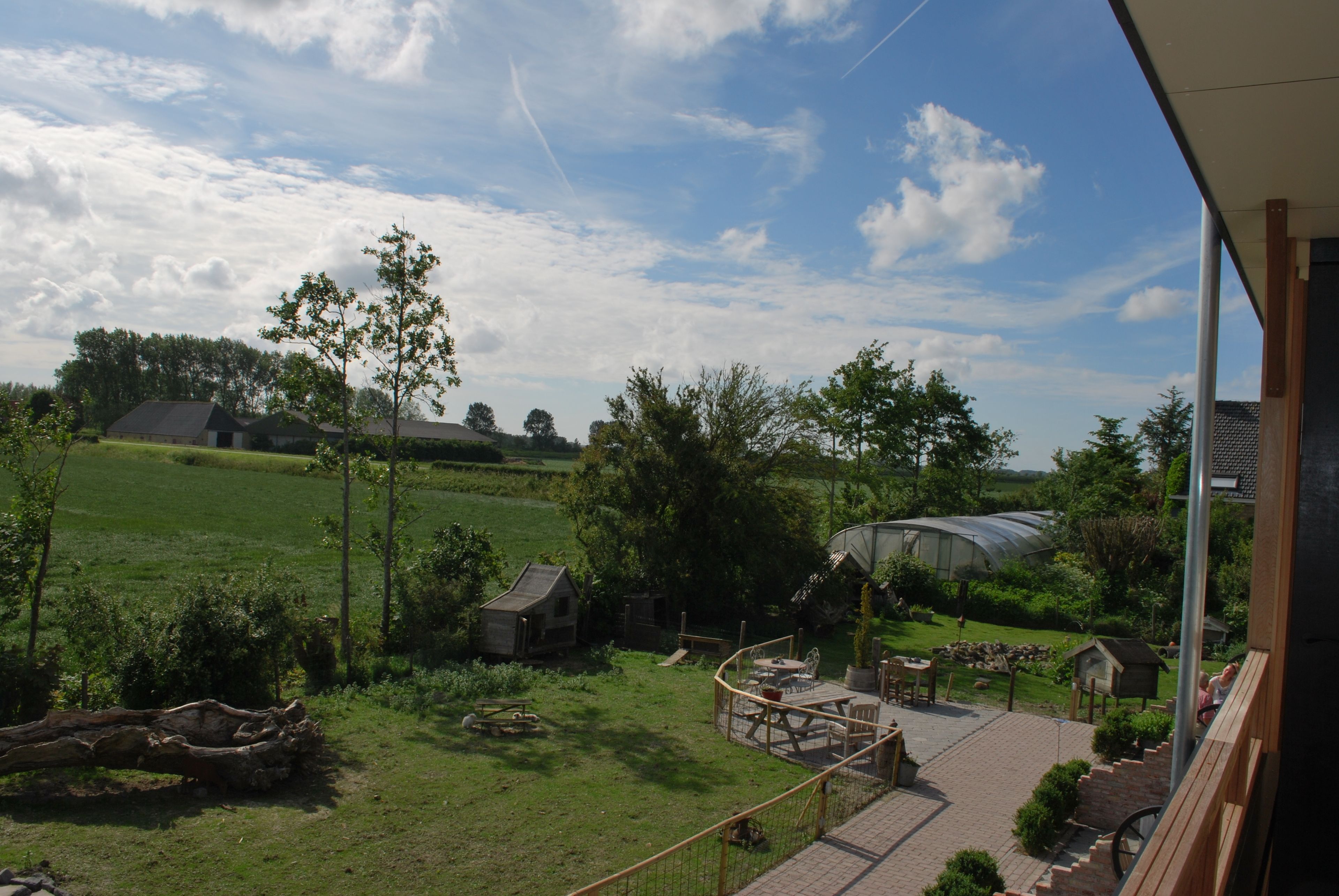 Vista de un paisaje rural con una terraza de madera, un pabellón y una casa pequeña.