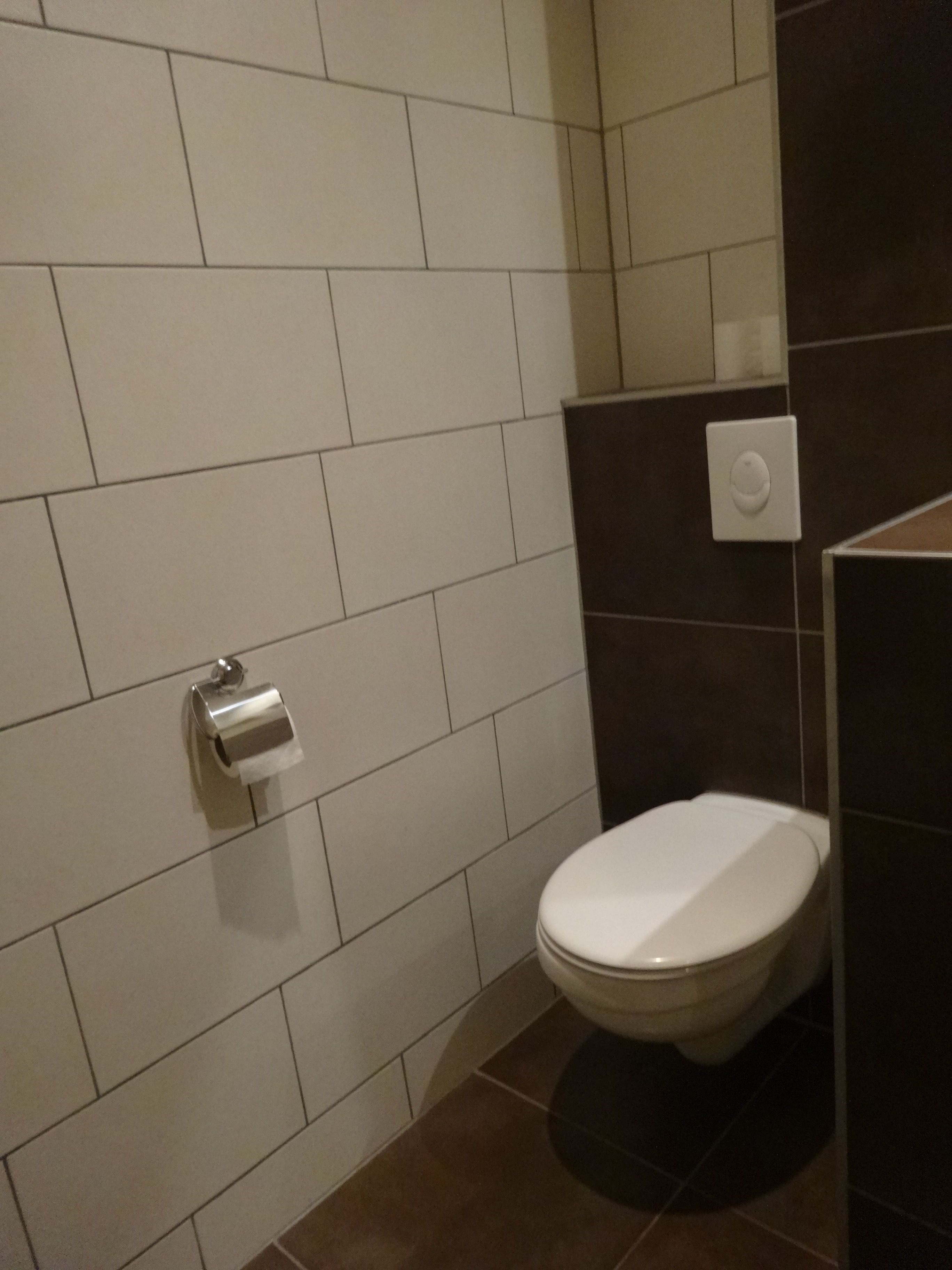 Een badkamer met een toilet, een papieren handdoekdispenser en een lichtschakelaar aan de muur.