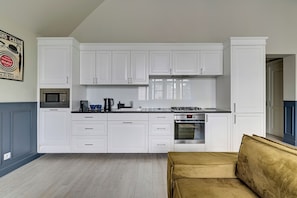 A modern kitchen with white cabinetry, a microwave, stove, and a sofa in the living area. - Lion Apartments - Scandi Love (Sopot)