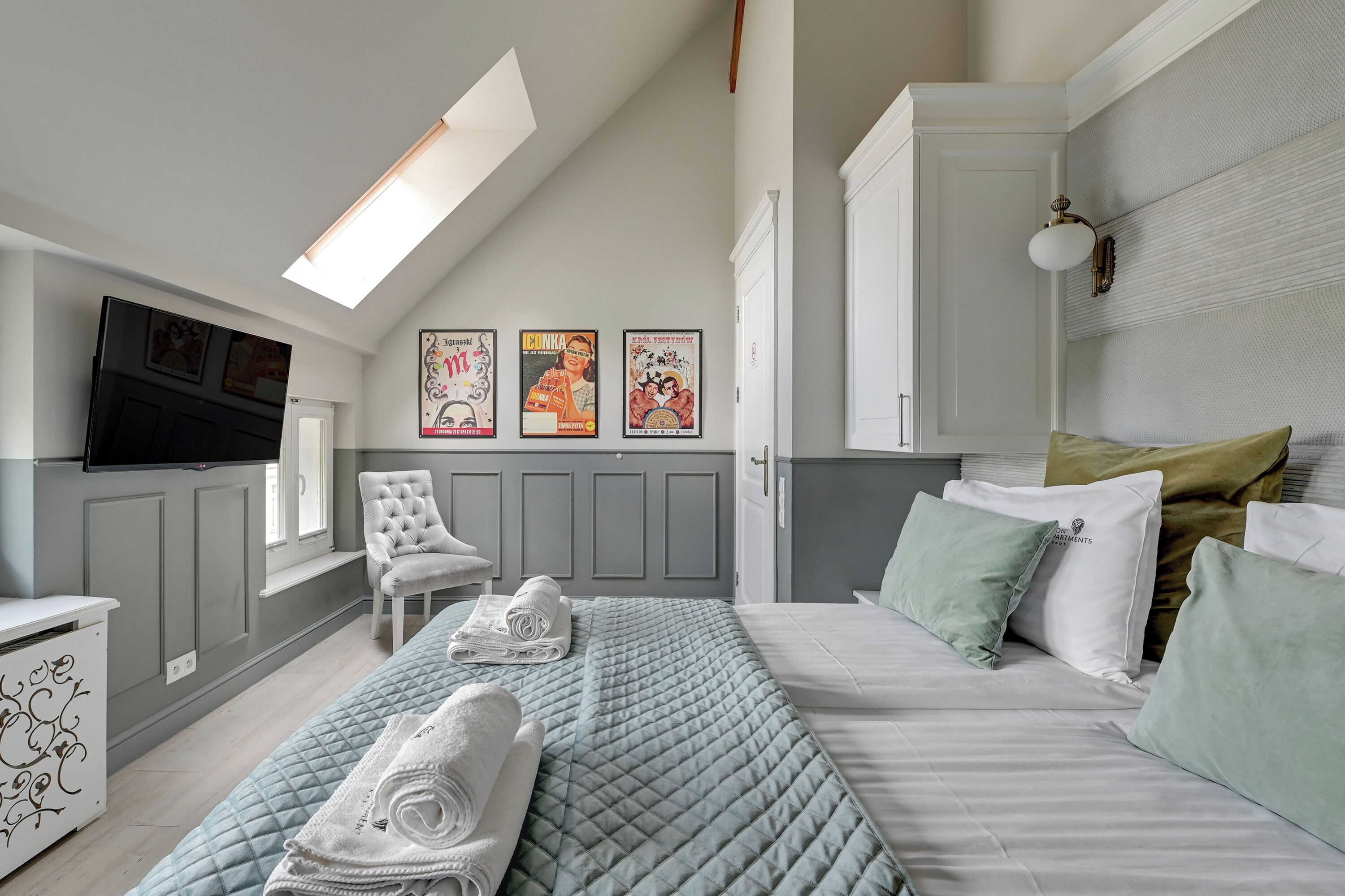 A bedroom with a bed, pillows, a chair, a TV, and wall art.