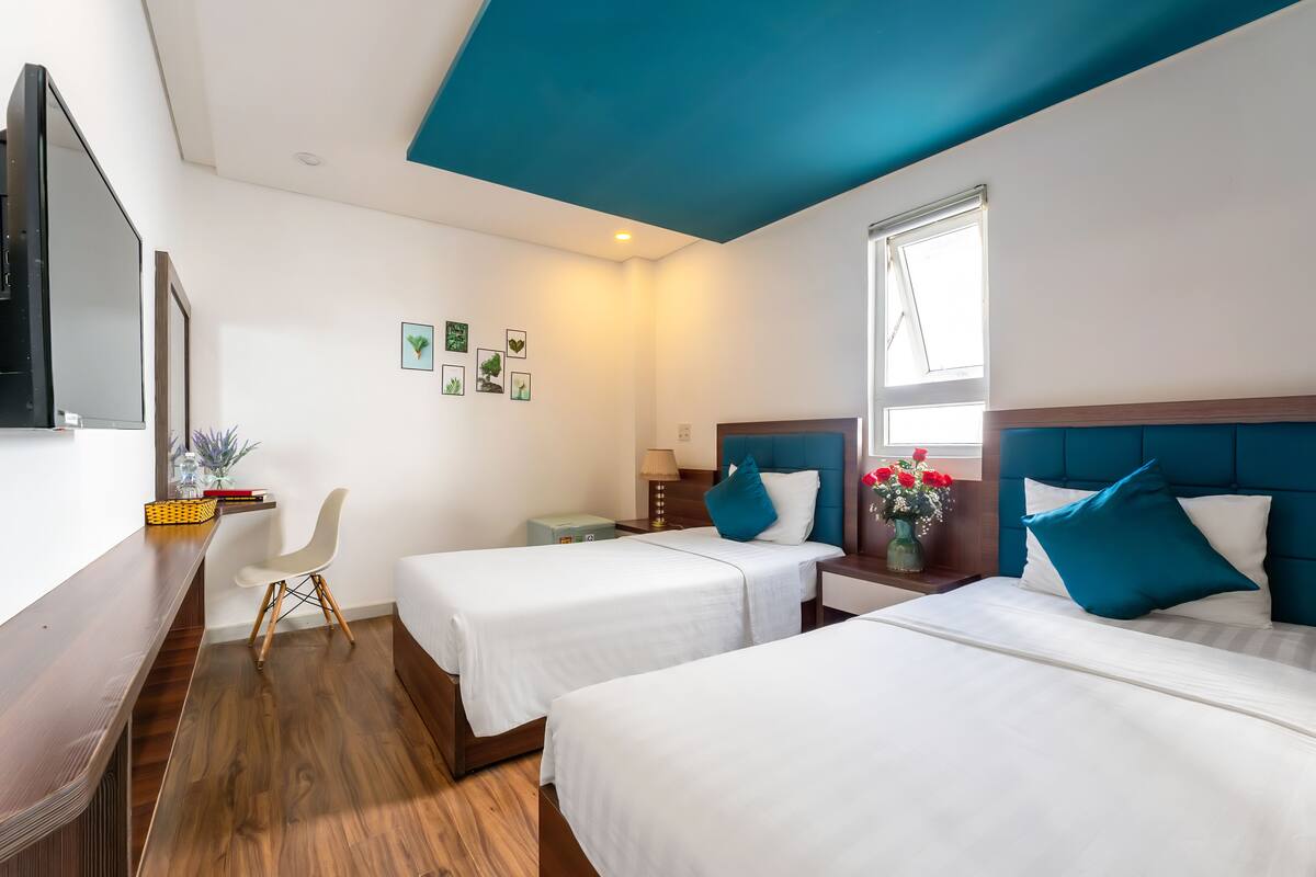 A hotel room with two beds, a desk, a chair, and a TV.
