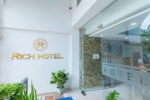 A reception area with a 'Rich Hotel' sign, a glass door entrance, and a potted plant. - Rich Hotel (Da Nang)