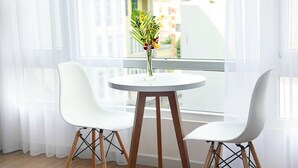 Una habitación con una mesa redonda, dos sillas blancas y un florero con flores.