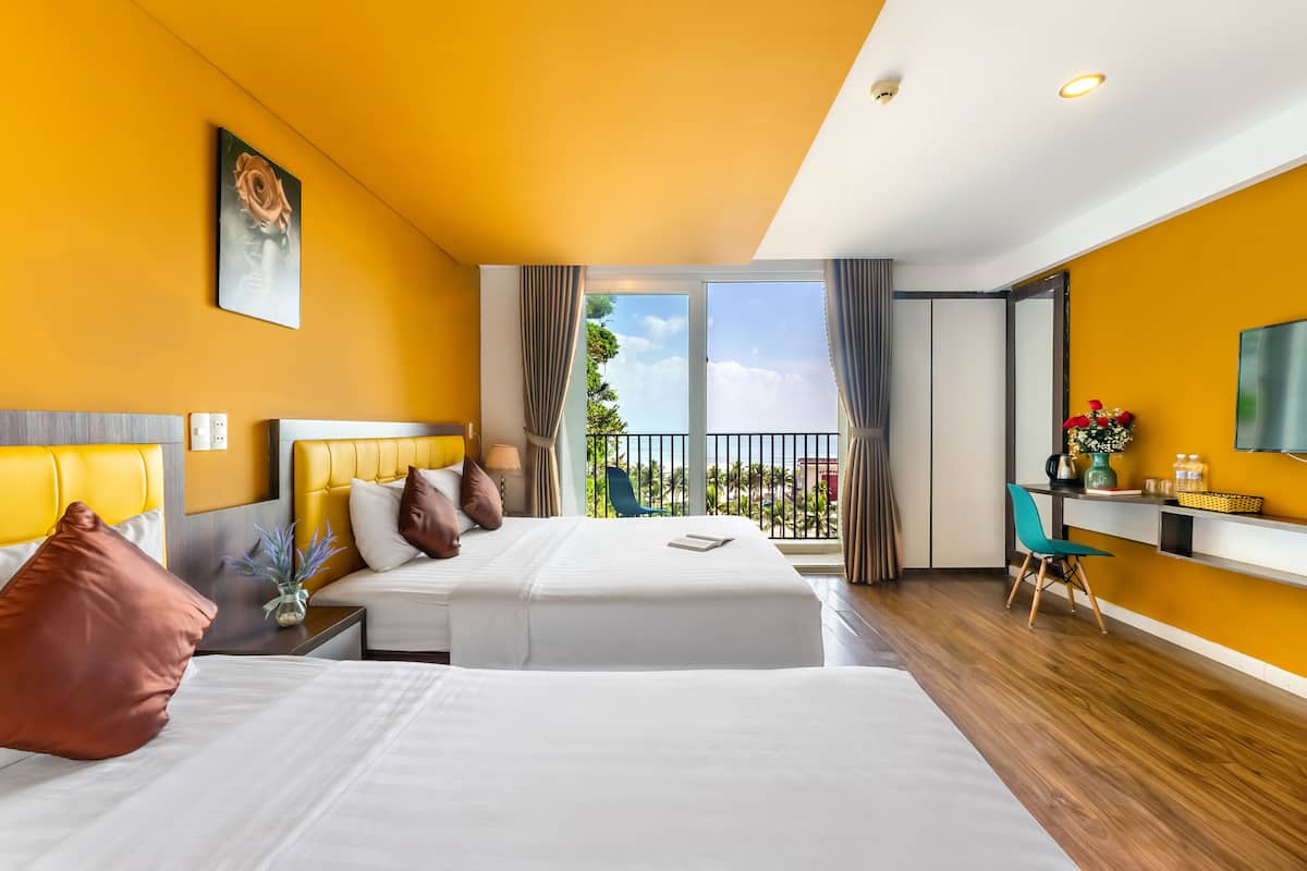 A hotel room with two beds, a balcony, a desk, and a TV.