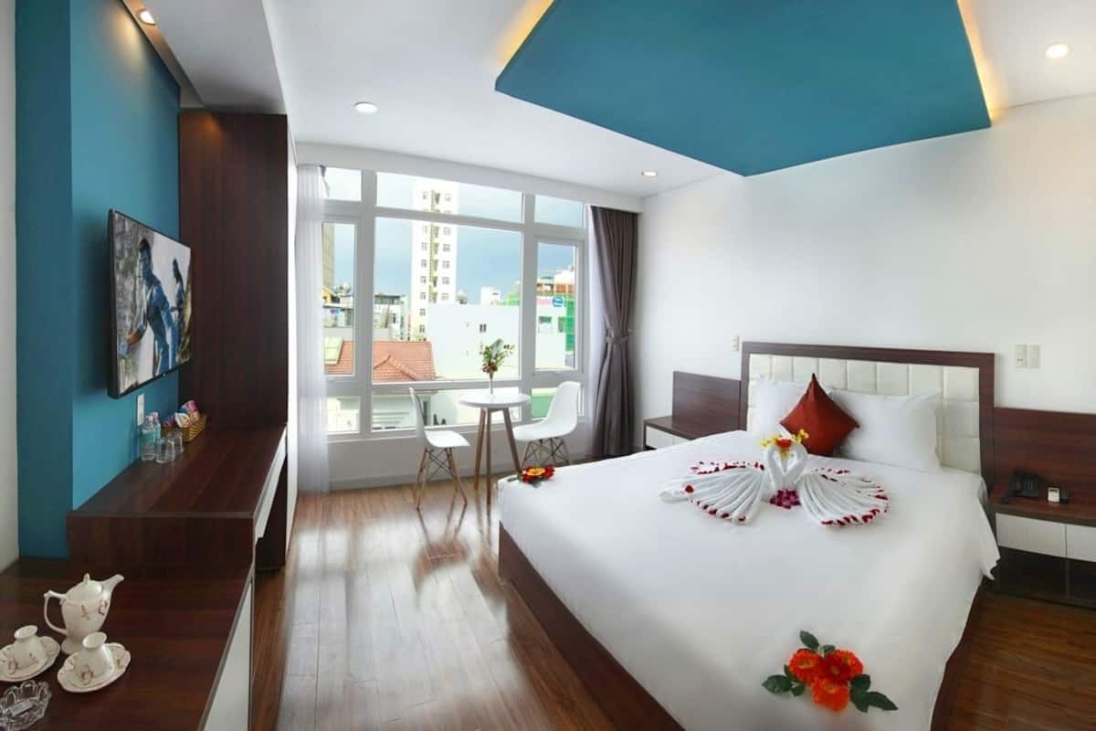 A hotel room with a large bed, a desk, a chair, and a window with a city view.