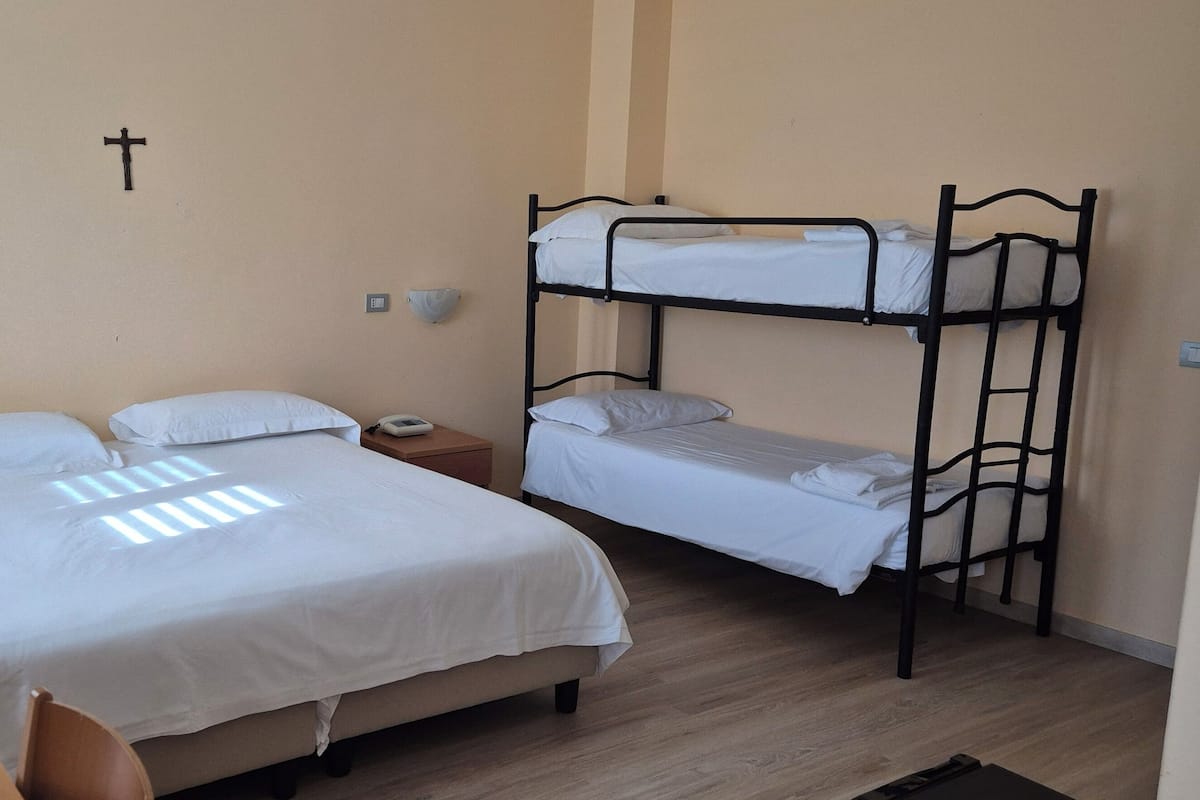 Un dormitorio con una cama doble, una cama individual, una mesita de noche con lámpara y un escritorio pequeño con una planta.