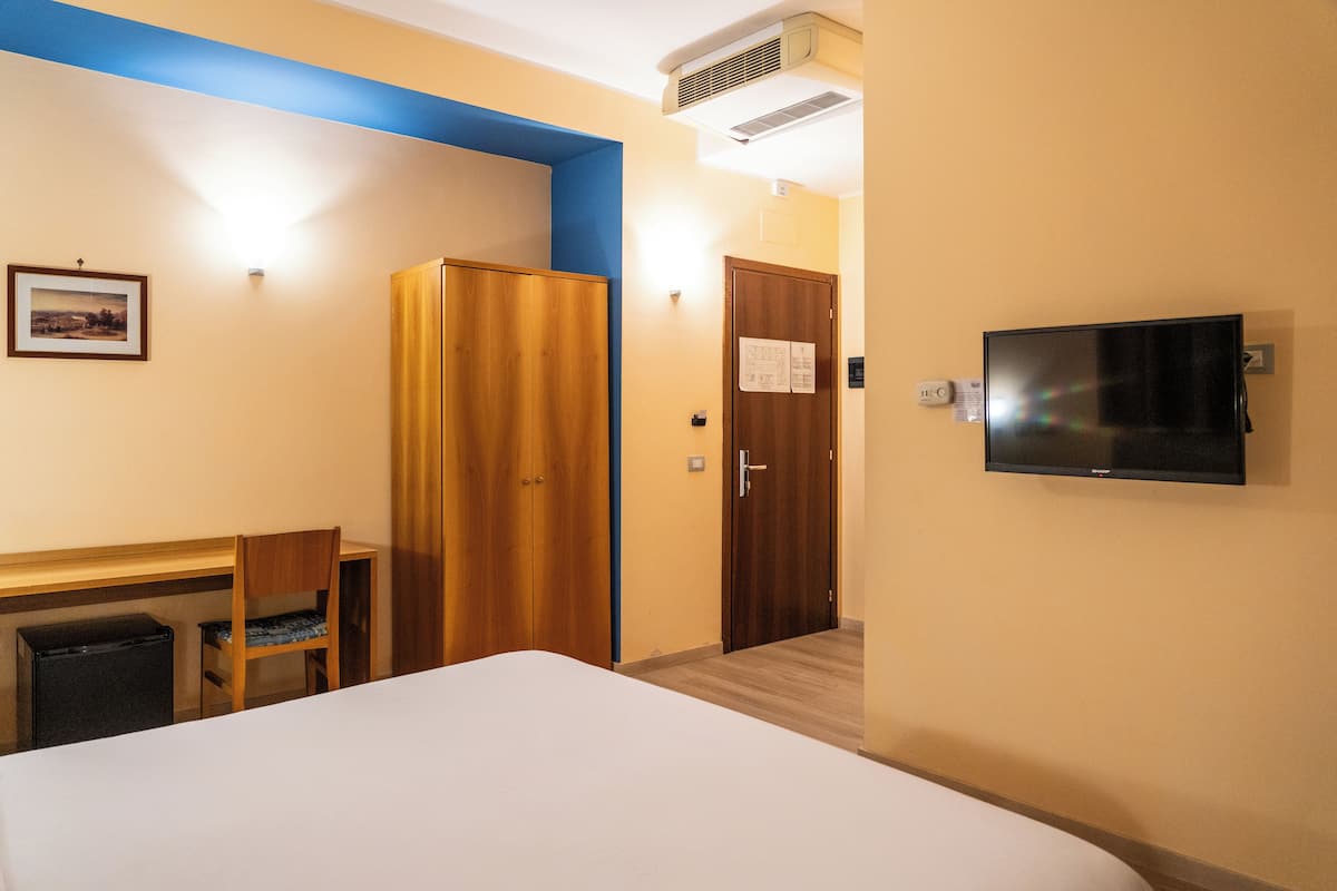 Una habitación de hotel con cama, escritorio, silla, armario, televisor y puerta.