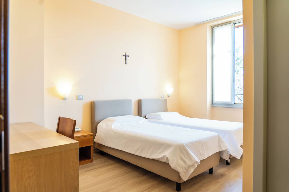 Un dormitorio con dos camas, un escritorio y una cruz en la pared.