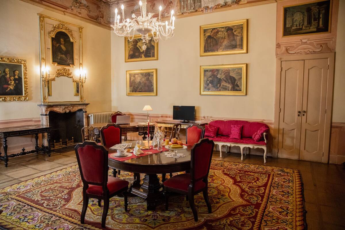 Un comedor con una mesa redonda, sillas rojas, una araña y un sofá rojo.