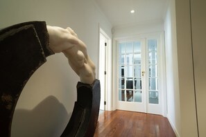 Un couloir orné d’une sculpture représentant un bras musclé, une porte blanche avec des panneaux de verre et un plancher en bois.