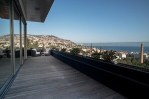 Un balcon offrant une vue sur le paysage urbain de la côte, avec un plancher en bois et des sièges d’extérieur.