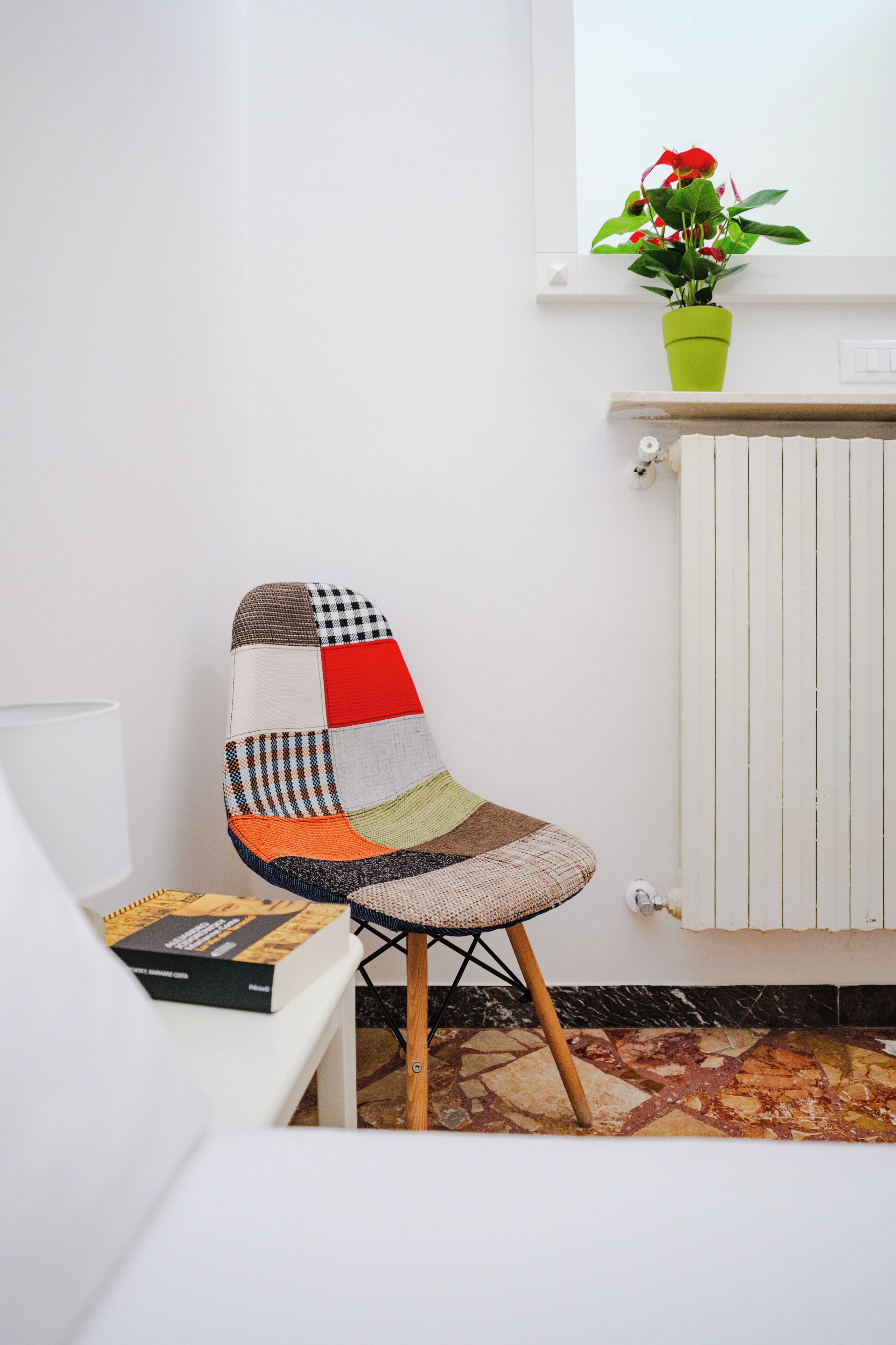 Una silla de patchwork con patas de madera, un radiador blanco y una planta en maceta sobre un alféizar.
