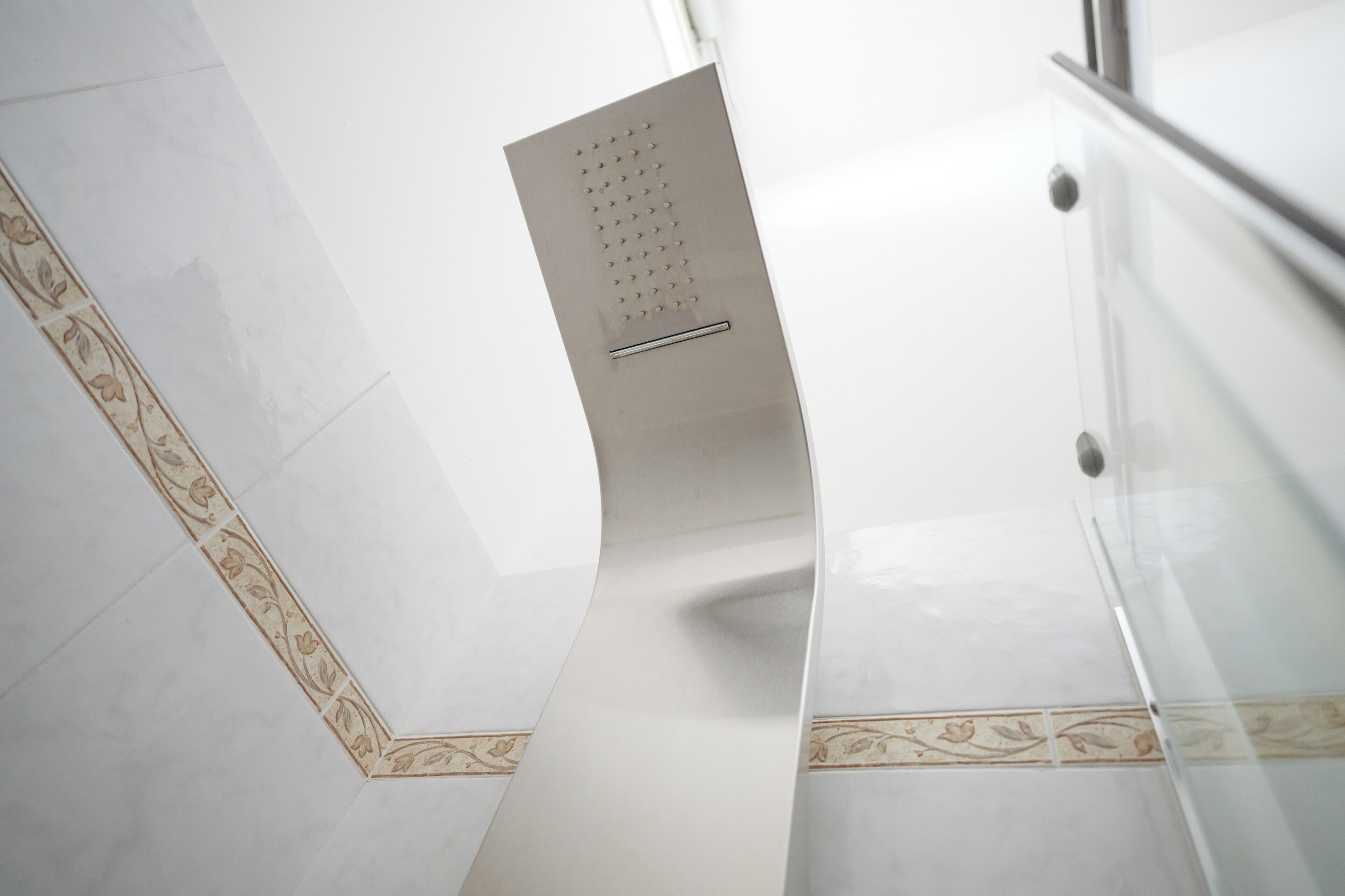 A modern interior with a curved glass railing, a patterned tile border, and a metallic handrail.