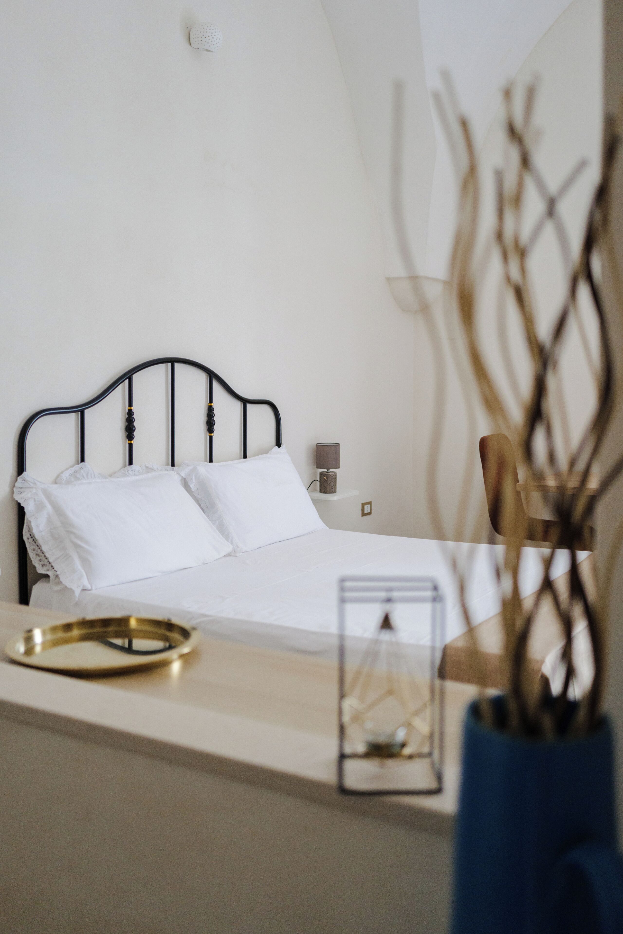 A neatly made bed with white linens, a bedside table with a lamp, and a decorative vase with branches.