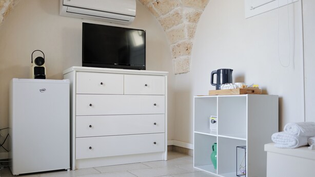 Habitación de hotel compacta con armario blanco, refrigerador pequeño, televisión de pantalla plana, cafetera y repisa con toallas.