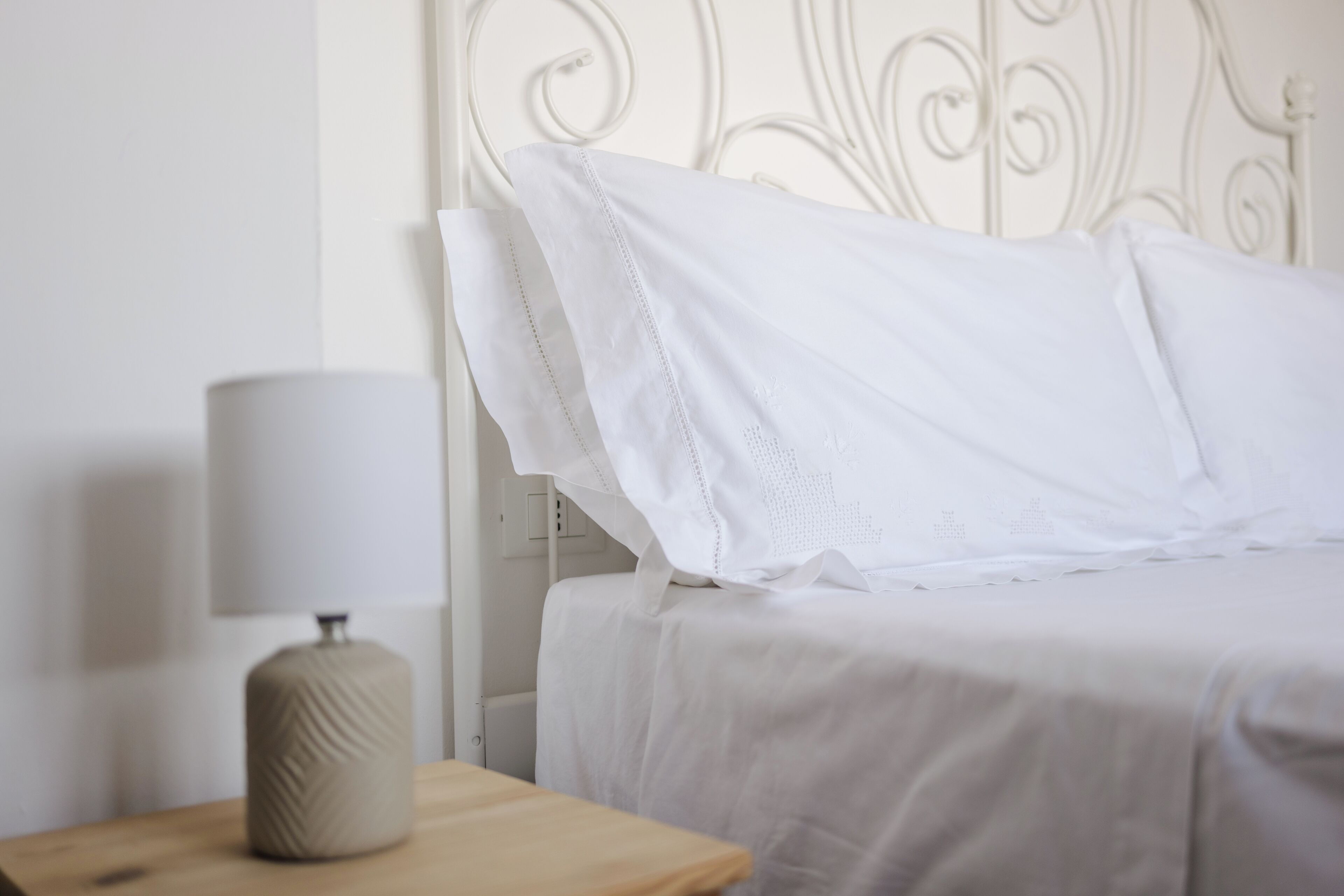 A neatly made bed with white linens, a bedside lamp, and a wooden nightstand.