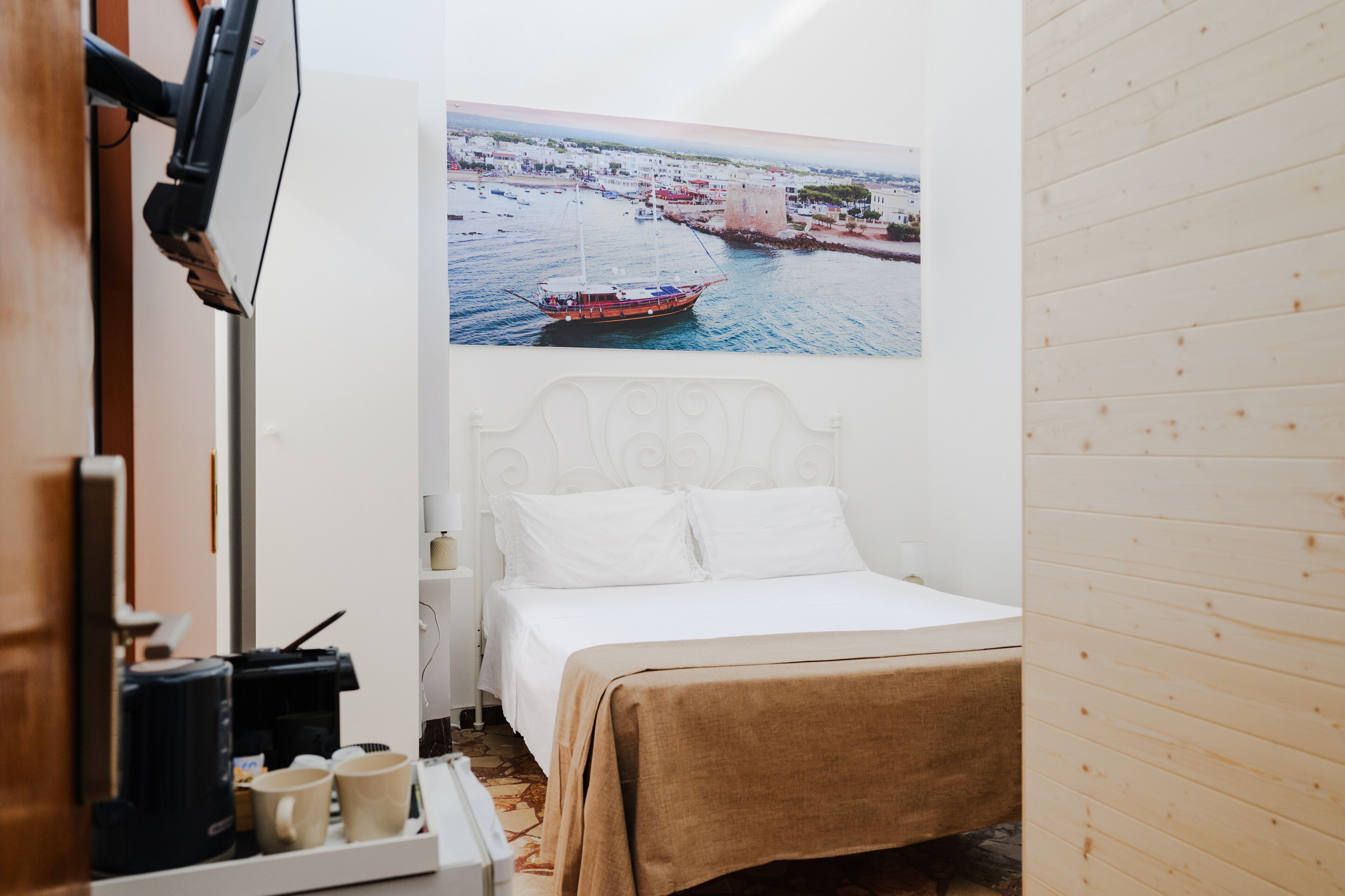 Une chambre à coucher avec un lit, une machine à café, une étagère avec des tasses et un tableau représentant un paysage côtier.