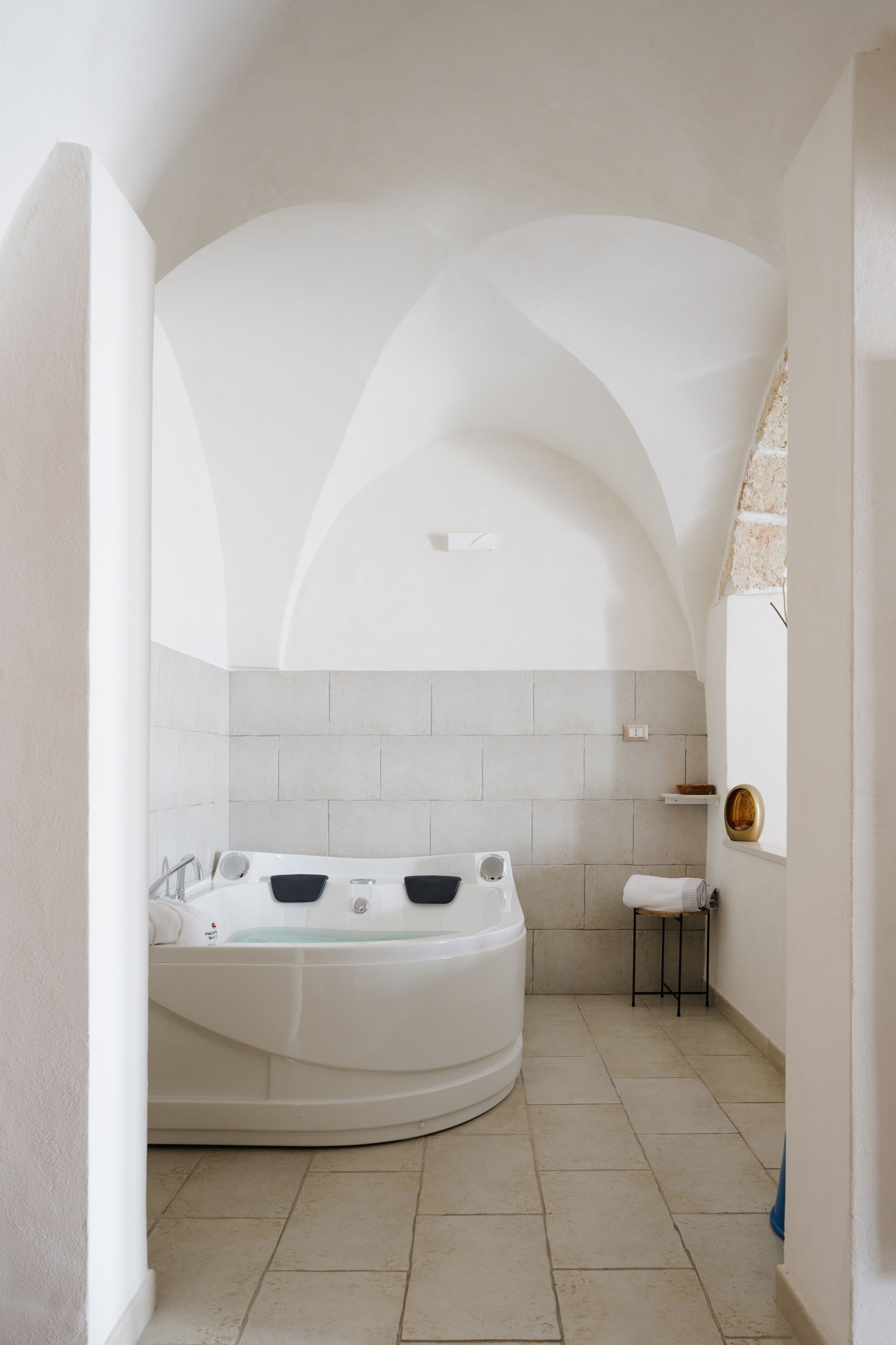 A modern bathroom with a freestanding bathtub, a small stool, and a tiled floor.