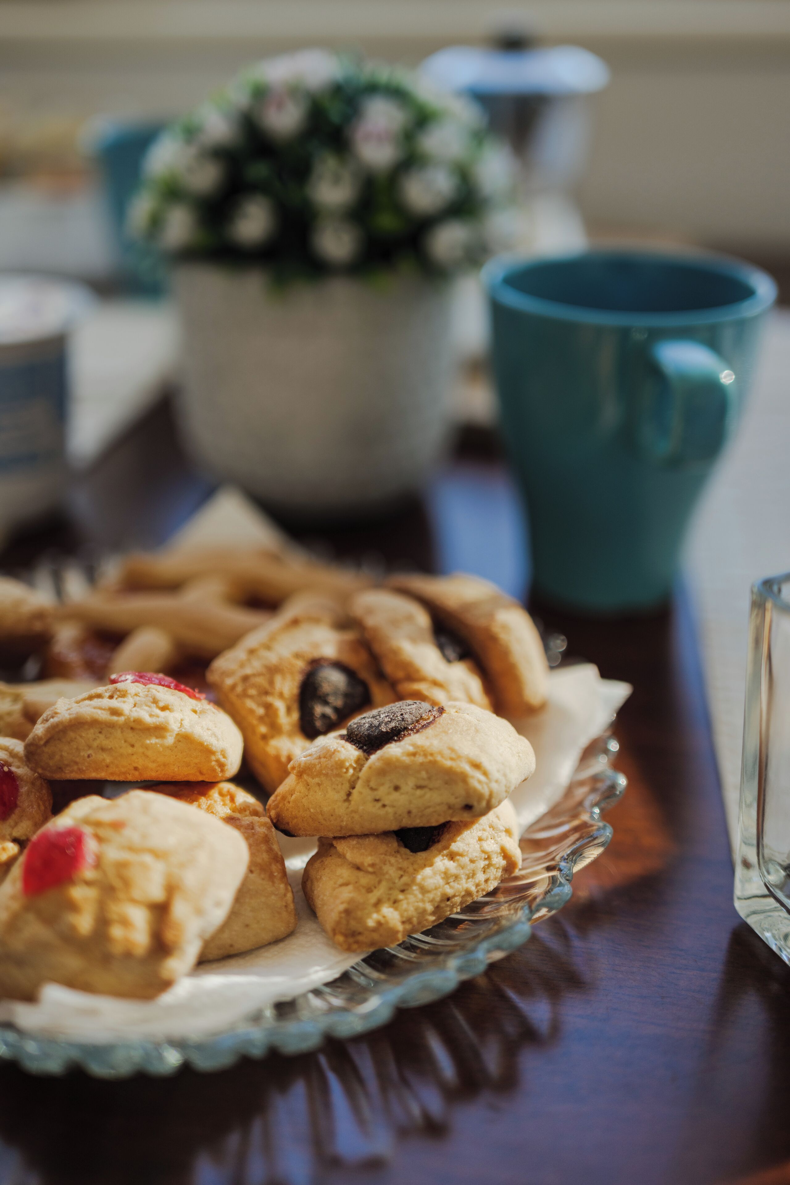 A glass plate with assorted pastries and a blue mug on a wooden table.