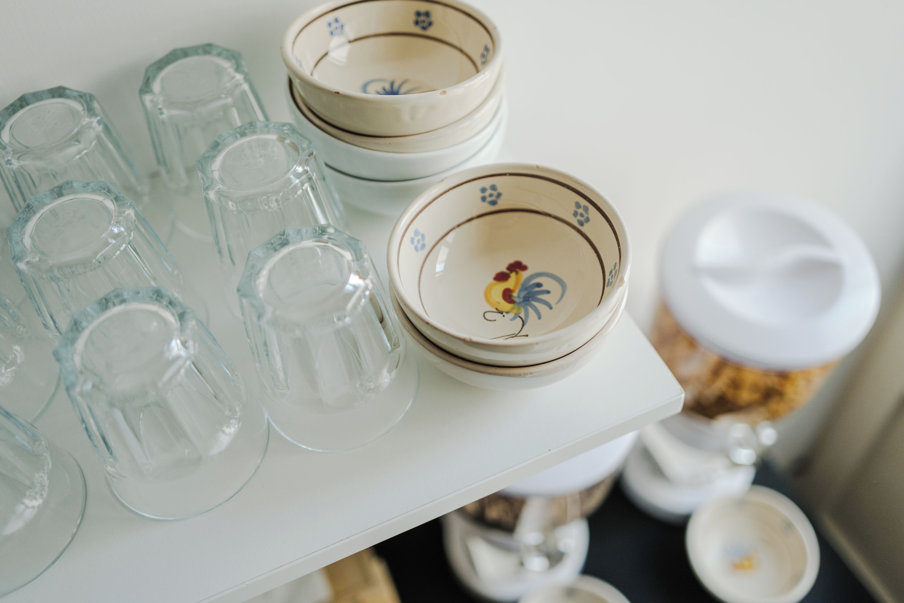 A white shelf with clear glass tumblers and ceramic bowls with floral designs.