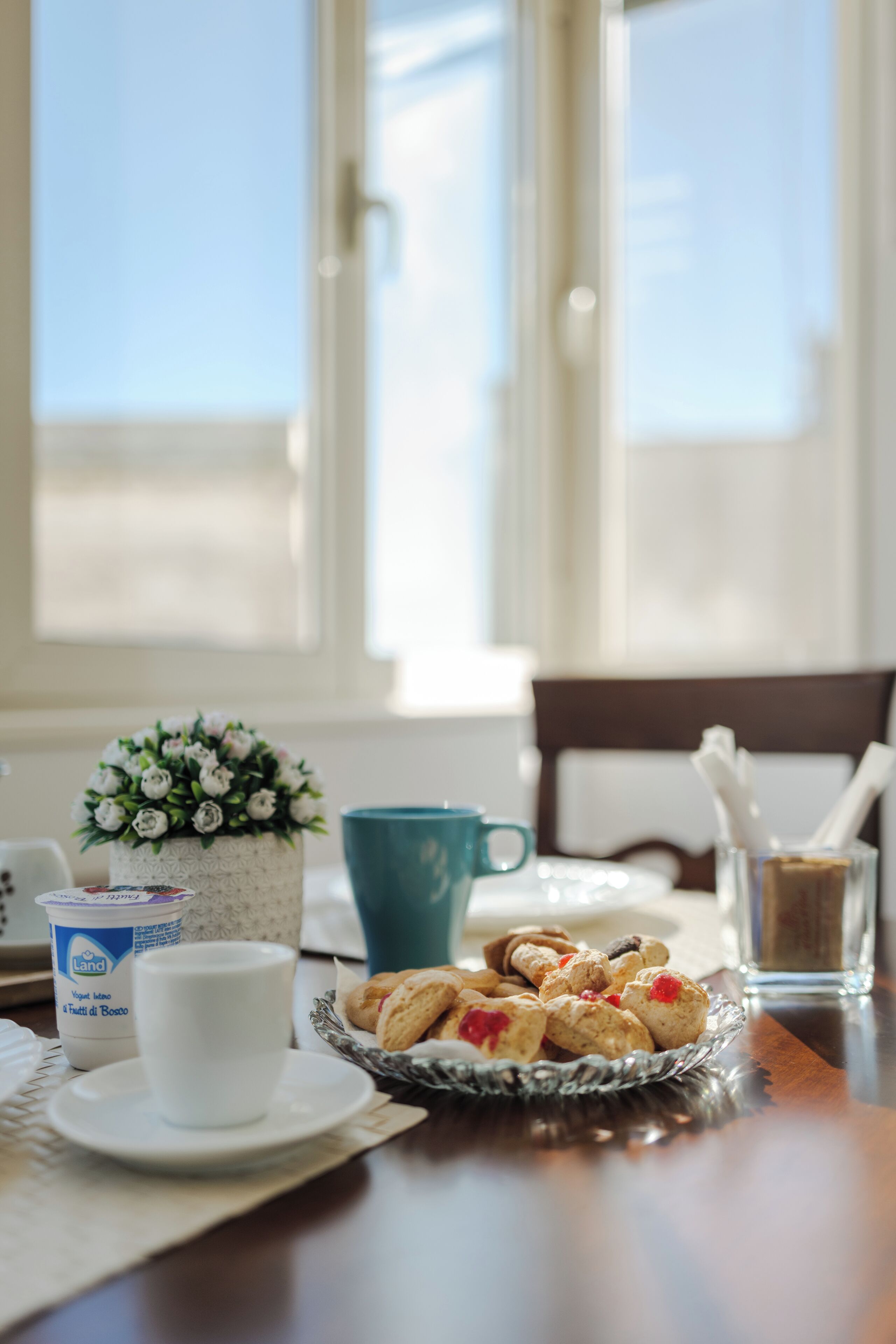 A breakfast table with a cup, a bowl of pastries, a small potted plant, and a glass of water.