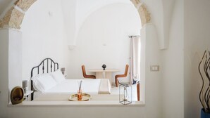 Un dormitorio con cama, mesita de noche y vistas a un comedor con mesa y sillas a través de un ventanal en arco.