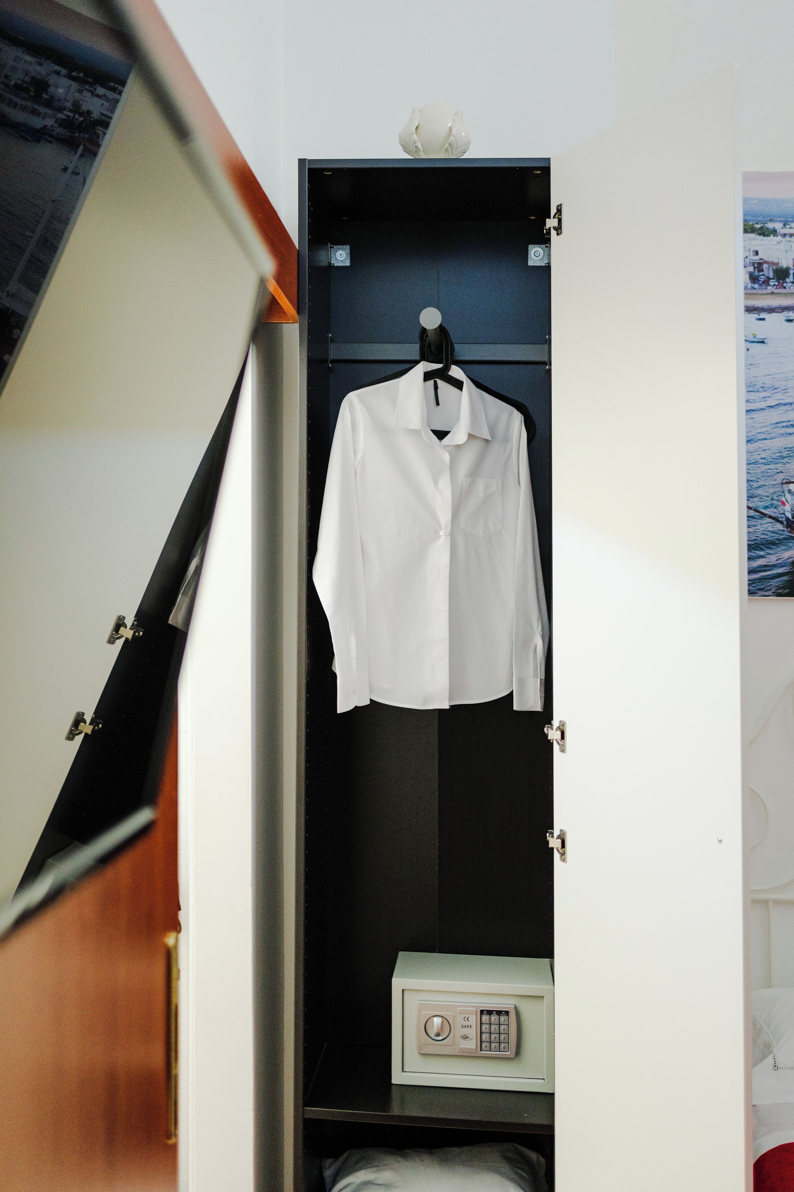 Una habitación con una cama, una camisa blanca colgada en una puerta y una caja fuerte.