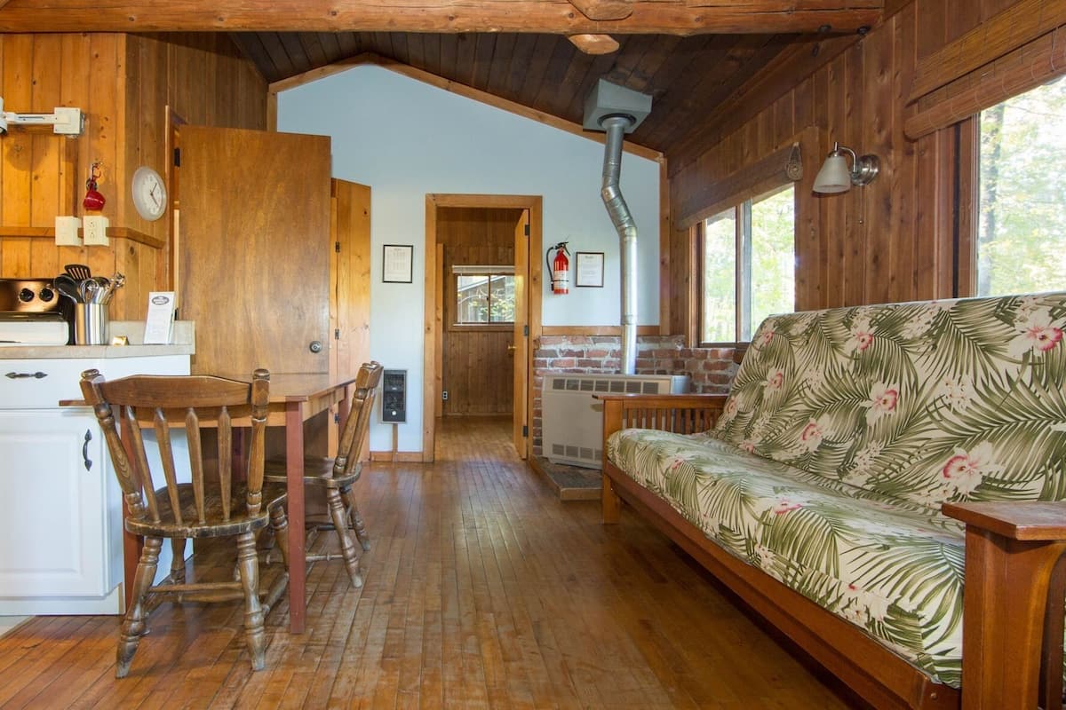 A wooden cabin interior with a dining area, a sofa, and a kitchen.