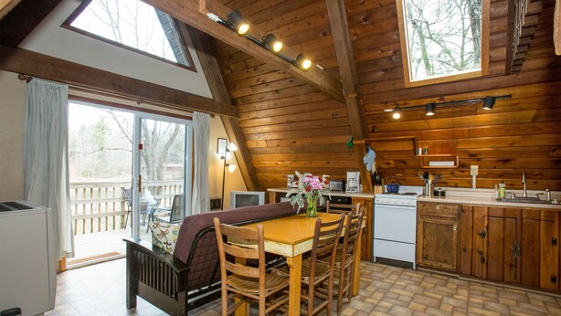 A wooden cabin with a dining area, kitchen, and a large window overlooking a deck. - Montfair Resort Farm (Crozet)