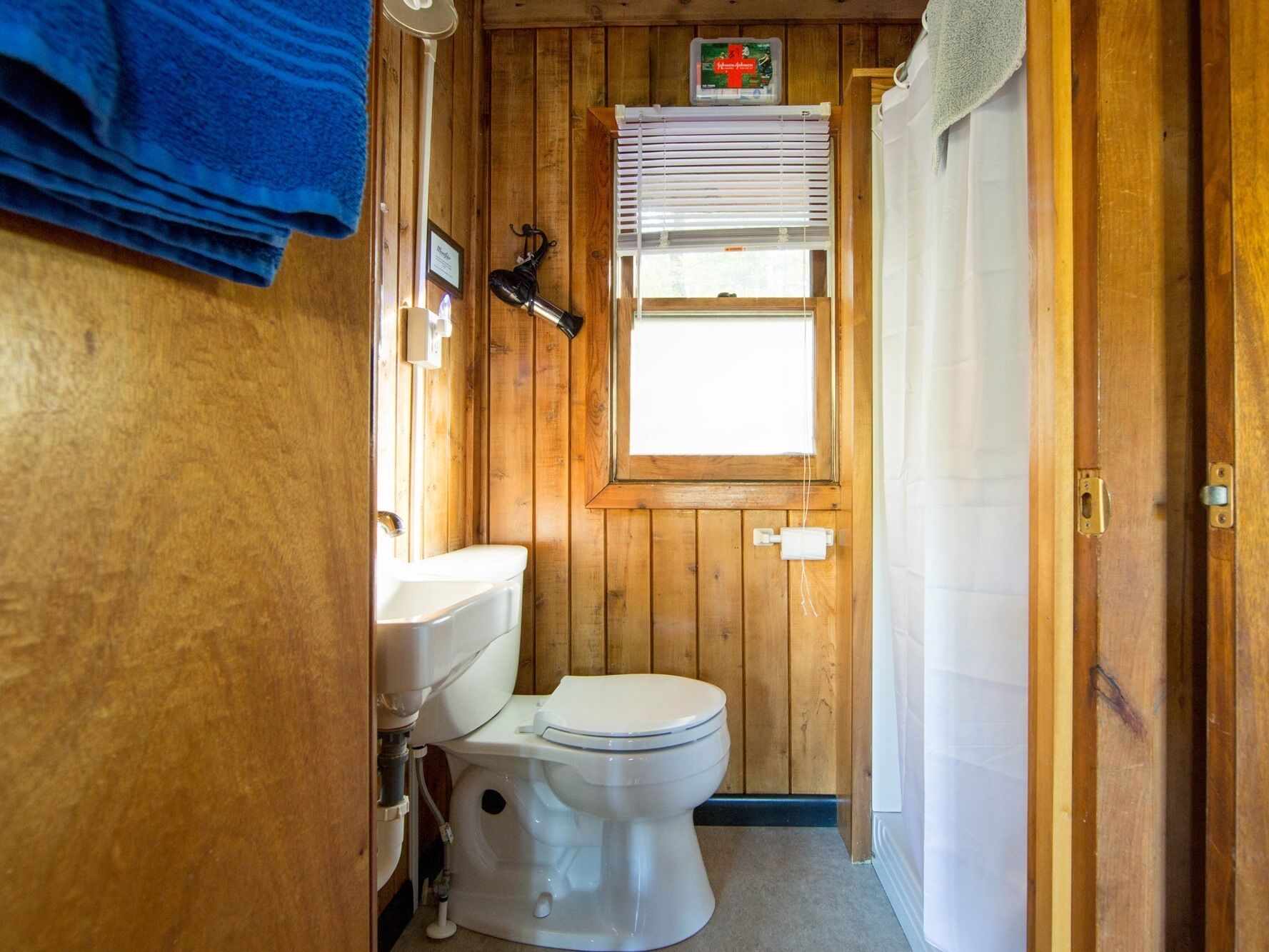 Un baño con paneles de madera, un inodoro, una ventana con persianas y un perchero para toallas.