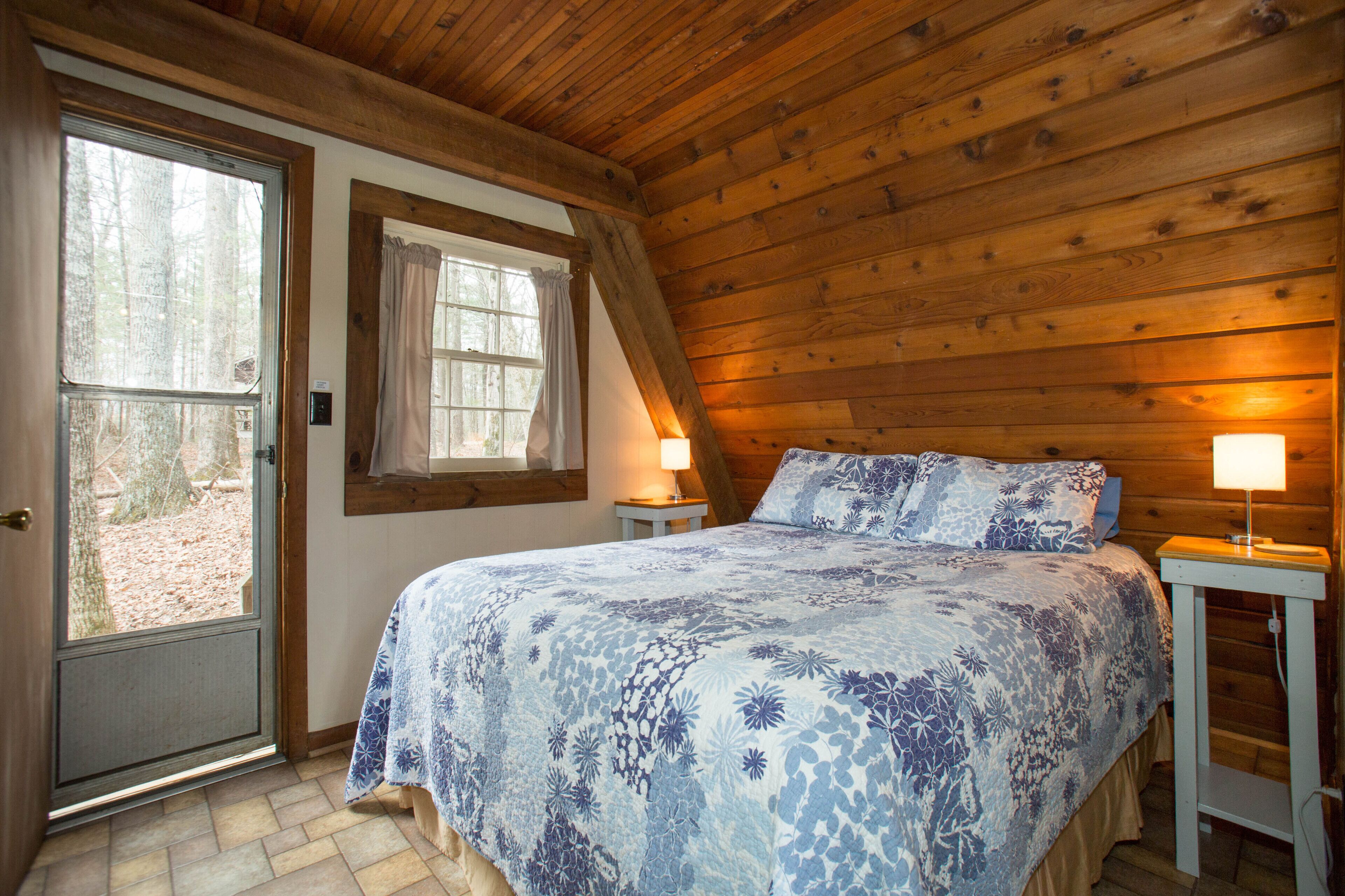 Un dormitorio con techo de madera, una cama con colcha floral, dos lámparas de noche y una ventana con cortinas.