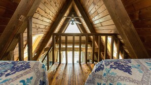 An attic bedroom with wooden beams, a sloped ceiling, and a bed with a floral bedspread. - Montfair Resort Farm (Crozet)