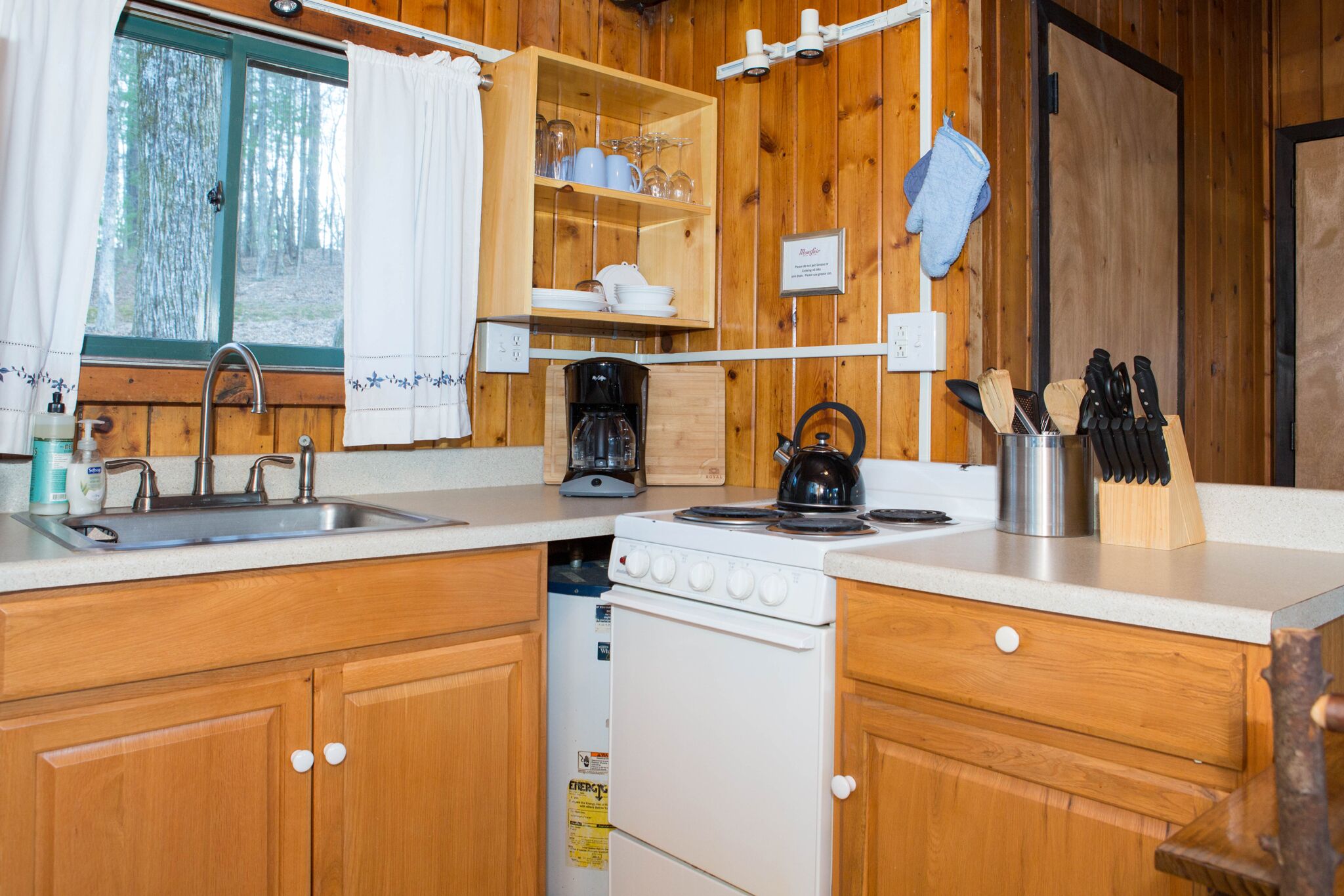 A wooden cabin kitchen with a sink, stove, and shelves with dishes and glasses.