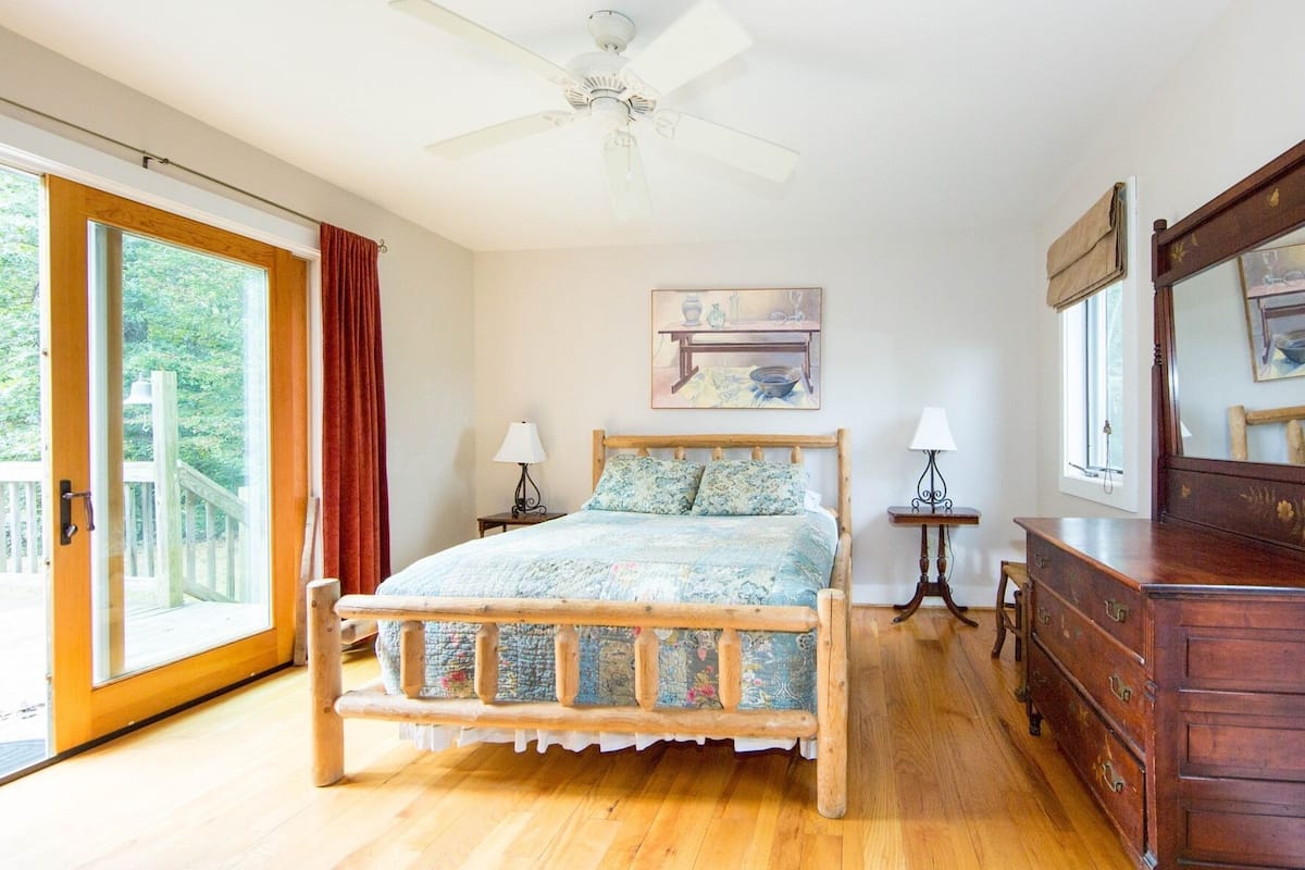 A bedroom with a wooden bed, a ceiling fan, a painting, a dresser, and a sliding glass door.