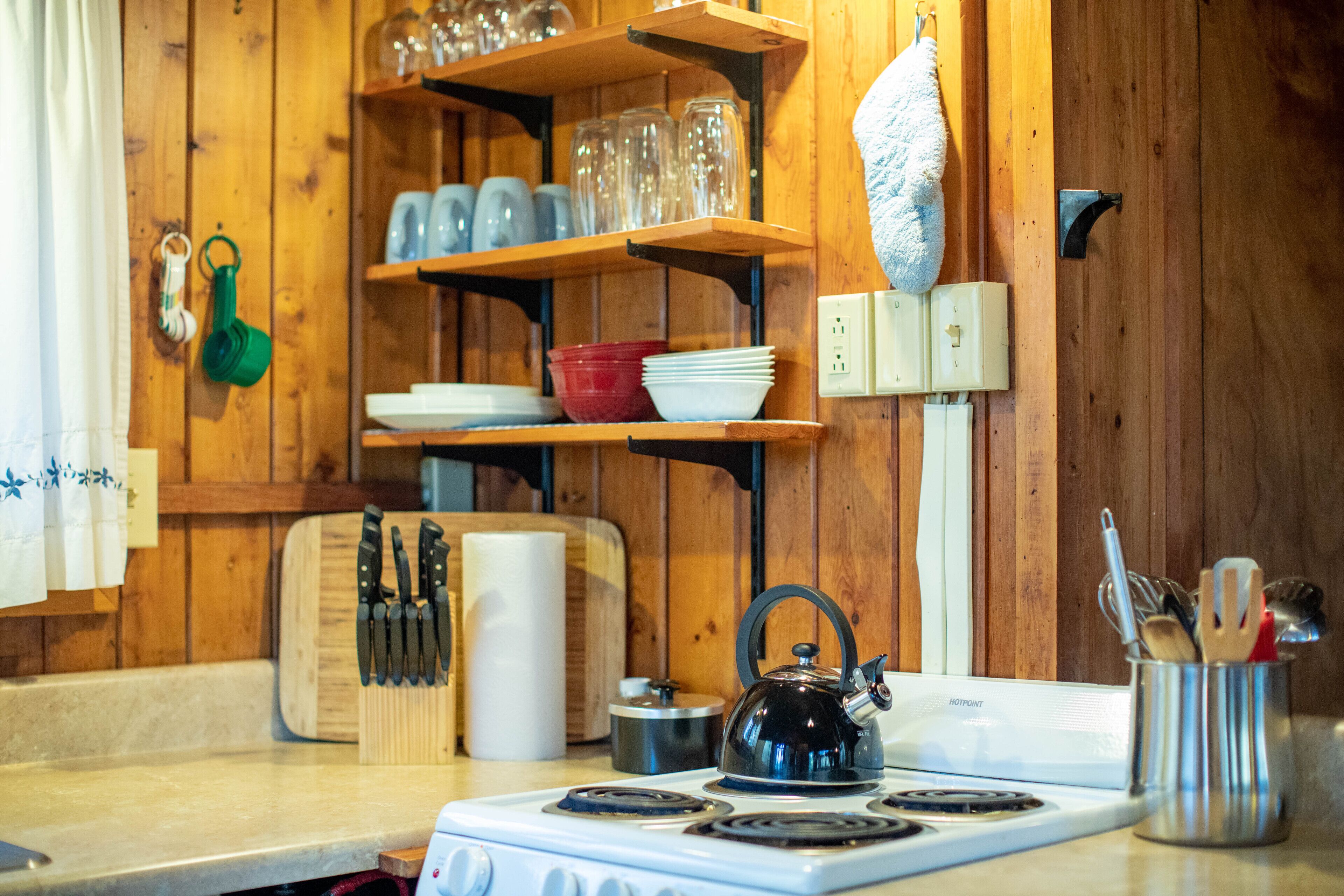 Una cocina con estantes de madera, un hervidor y diversos utensilios.
